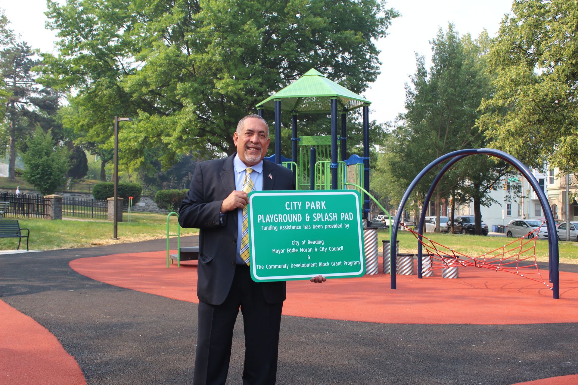 A man in a suit and tie is holding a sign in front of a playground.
