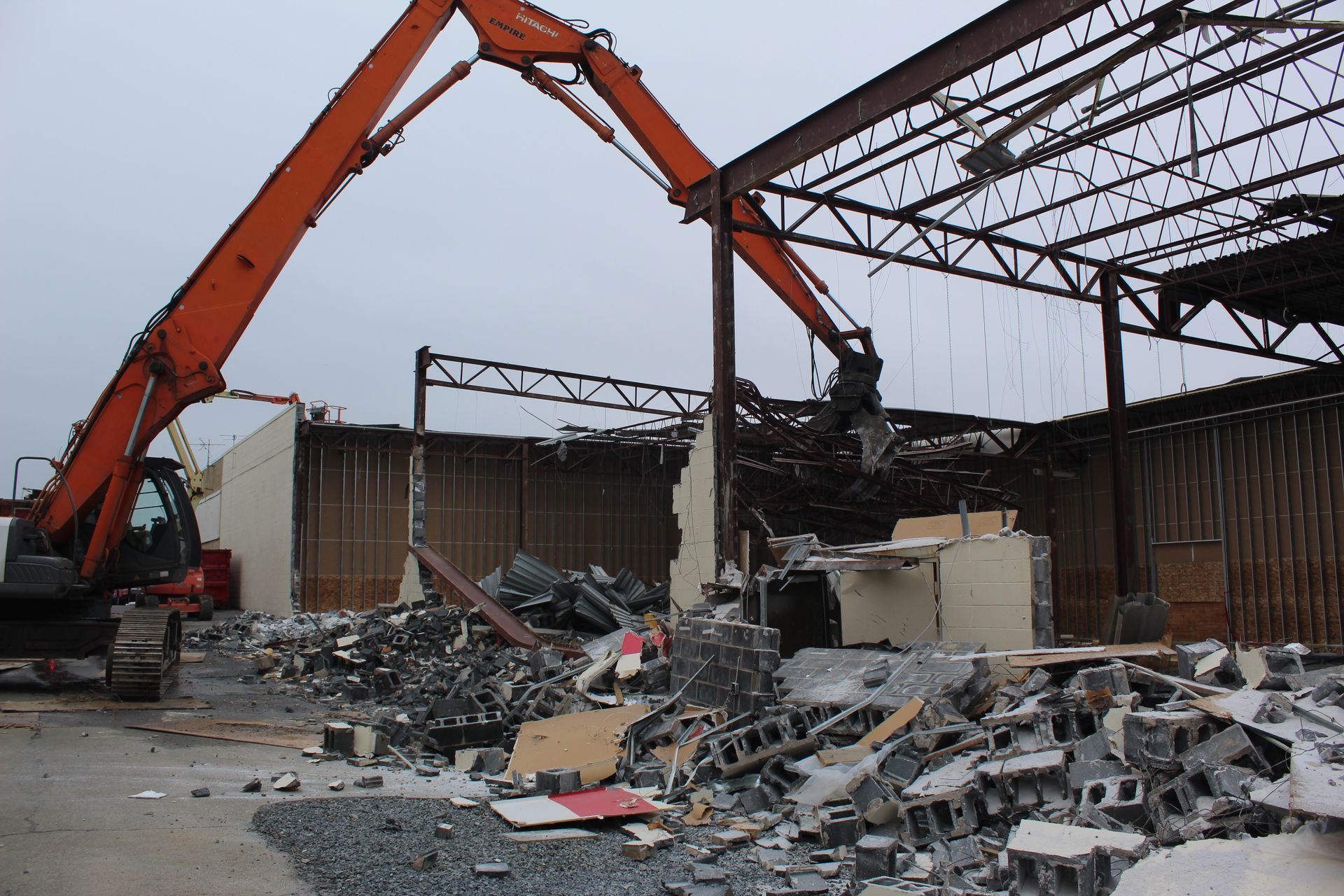 A large orange excavator is demolishing a building