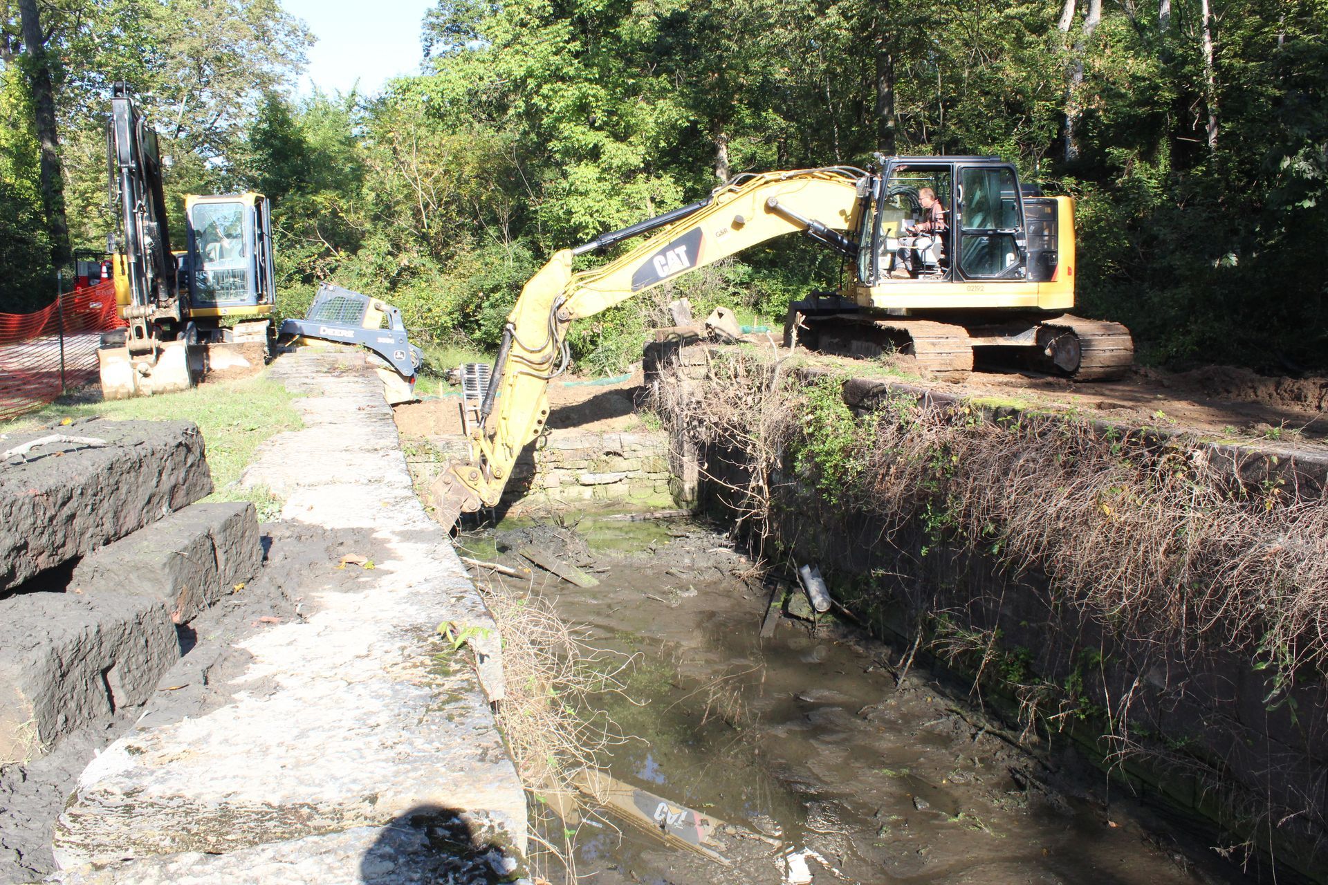 A yellow excavator is digging a stream in the woods