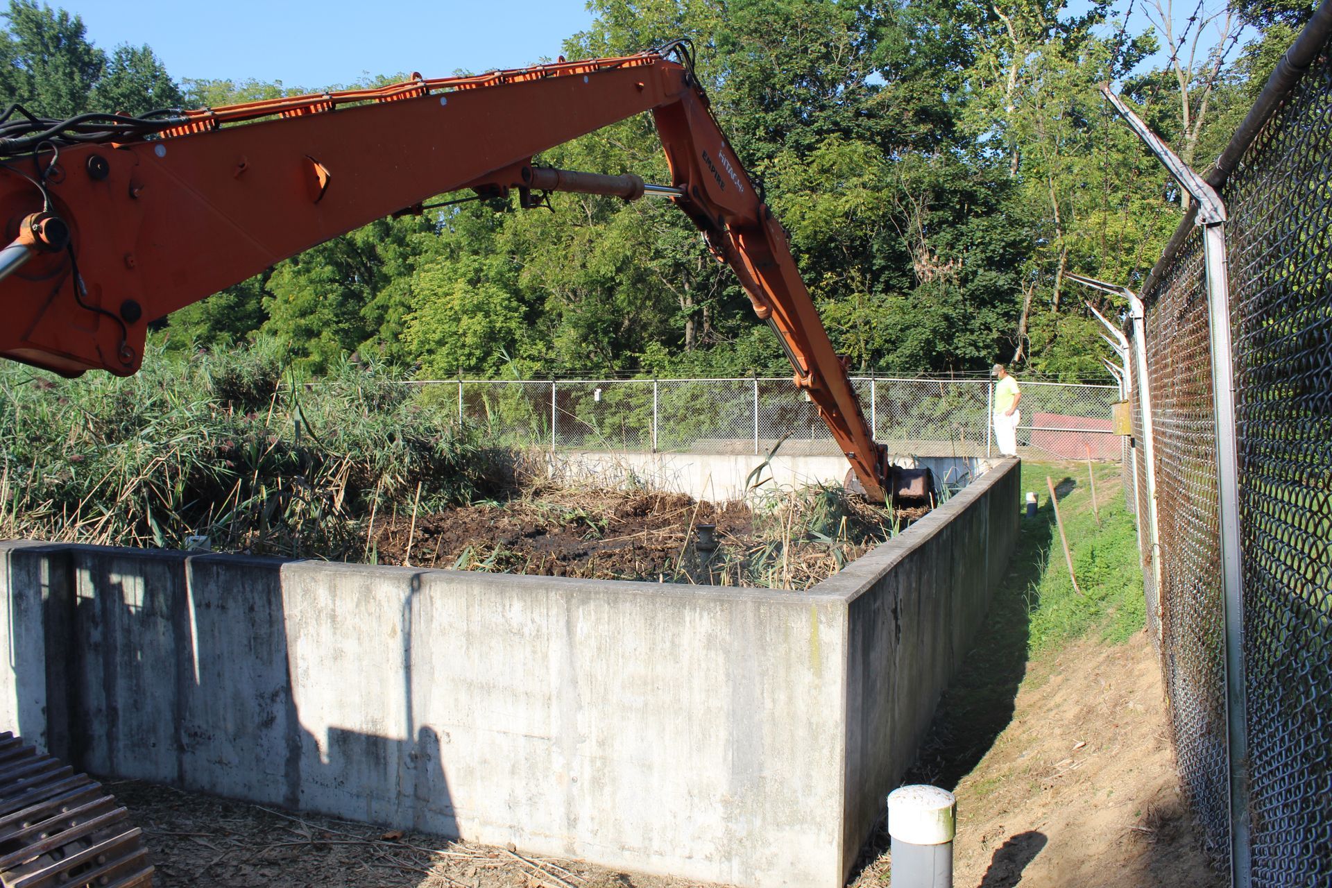 Using an excavator to remove sludge, reeds and filtration media from reed beds at a wastewater treatment plant.