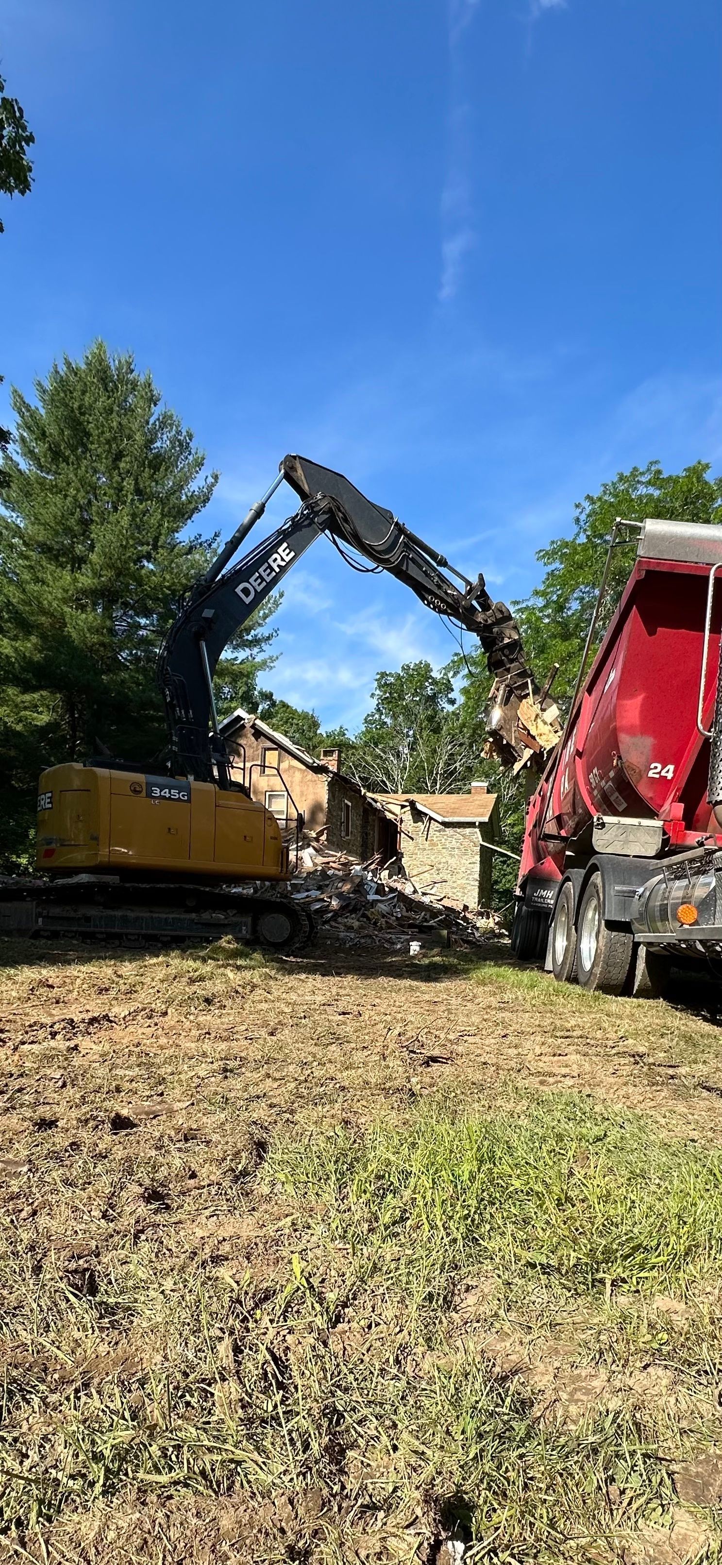 A bulldozer is demolishing a building in a field next to a dump truck.