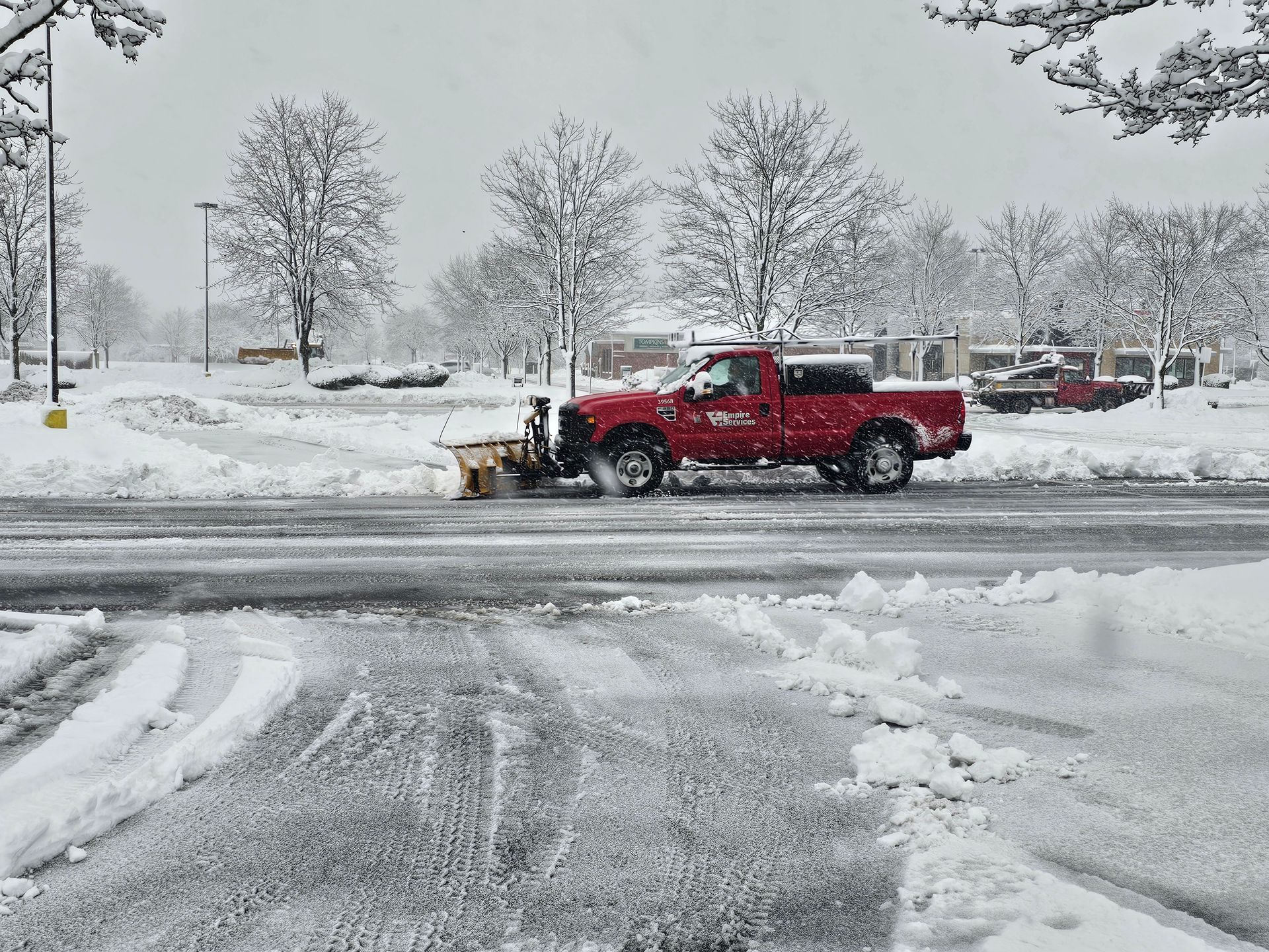 A red truck is plowing snow on the side of the road.