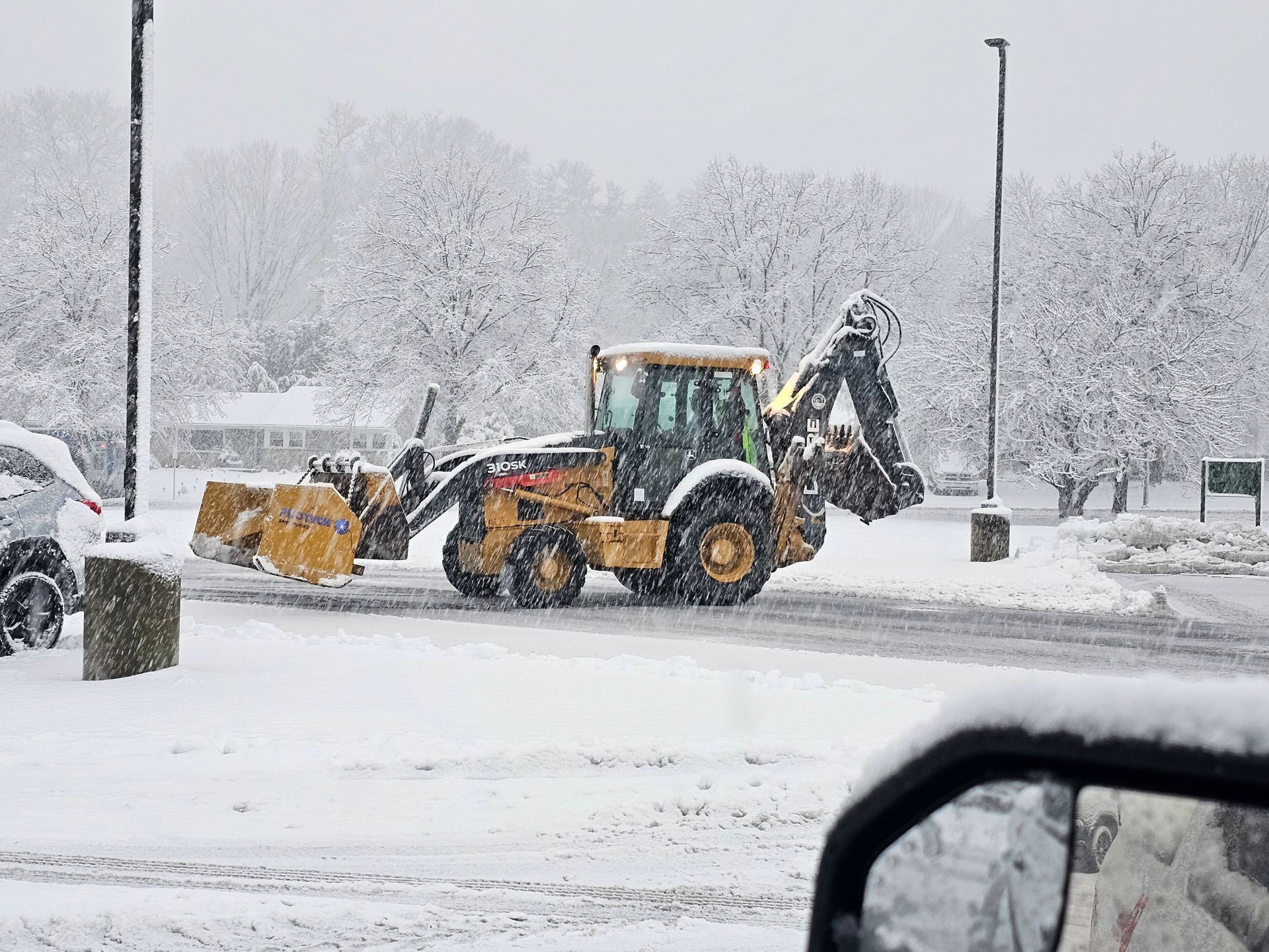 A yellow tractor is plowing snow in a parking lot.