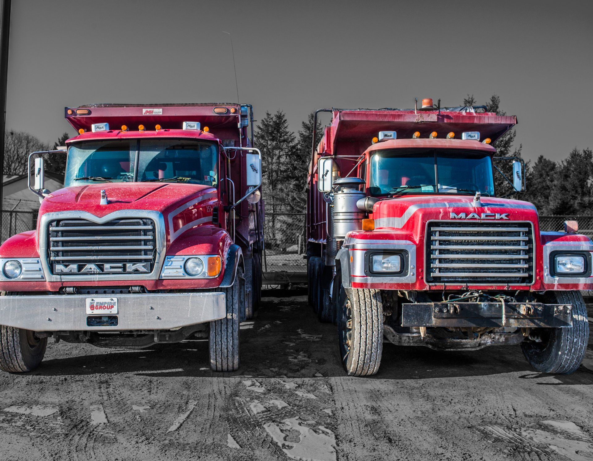 Two red mack dump trucks are parked next to each other
