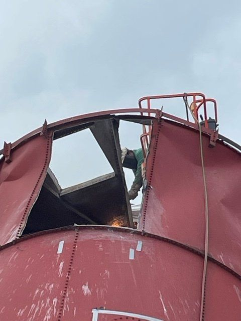 A man is welding on top of a red tank