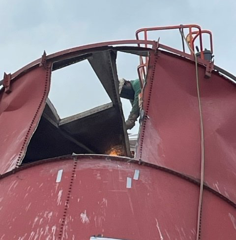 A man is welding on top of a large red tank.
