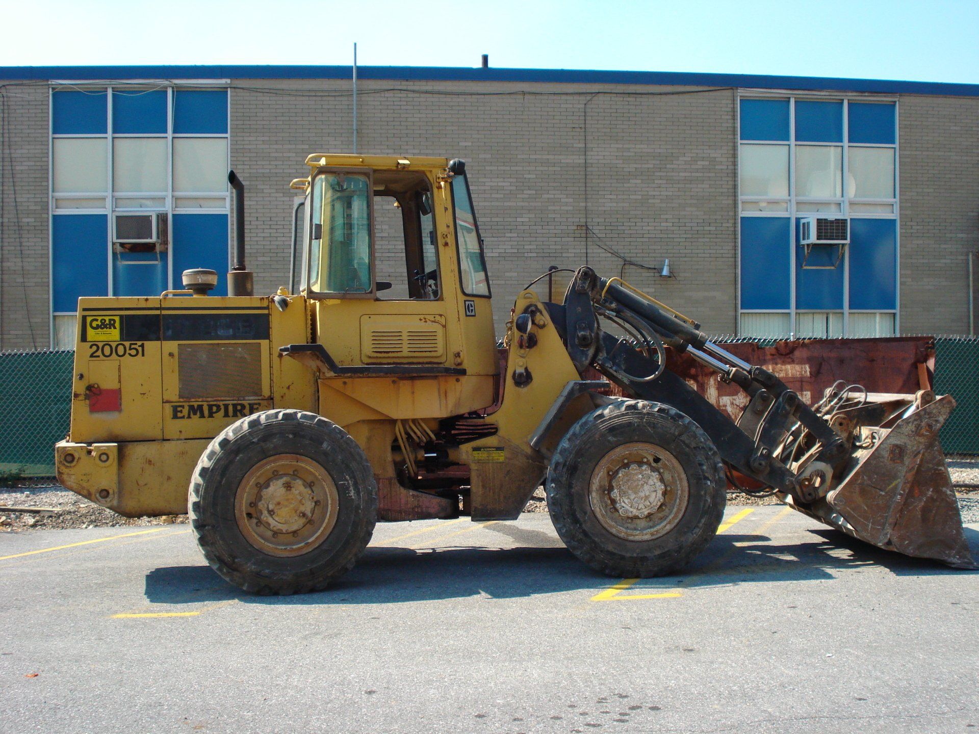 A yellow empire wheel loader is parked in front of a building