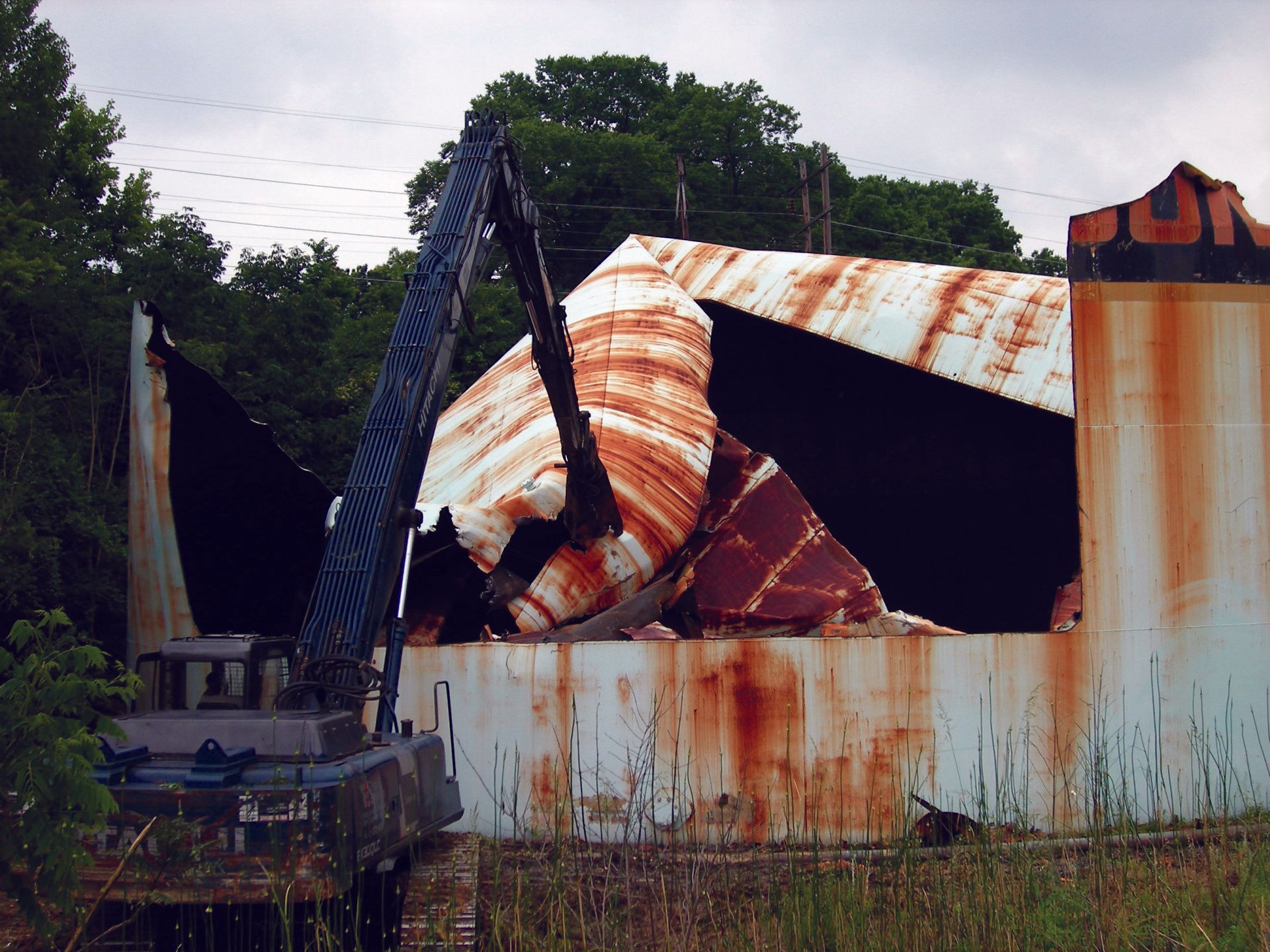 An old rusty building is being demolished by a crane