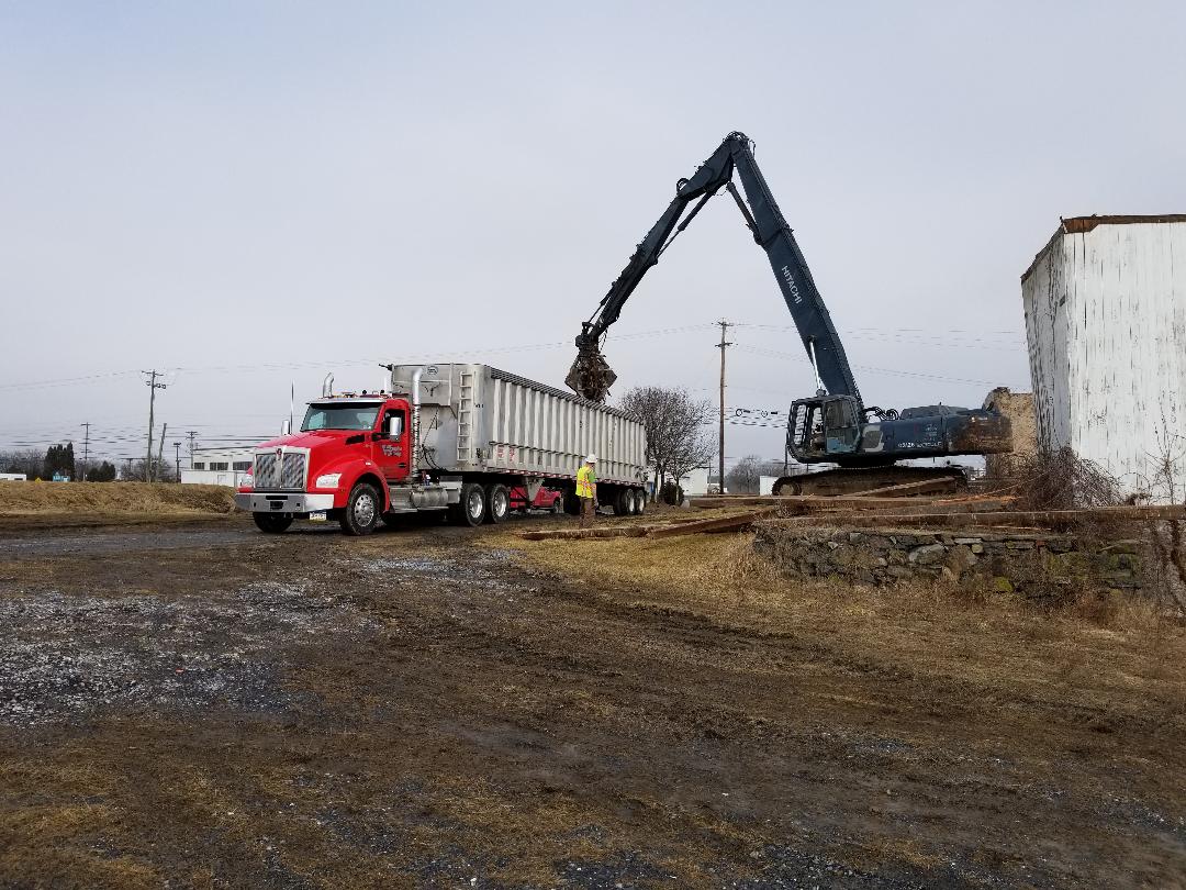 A red truck is driving down a dirt road next to a large excavator.