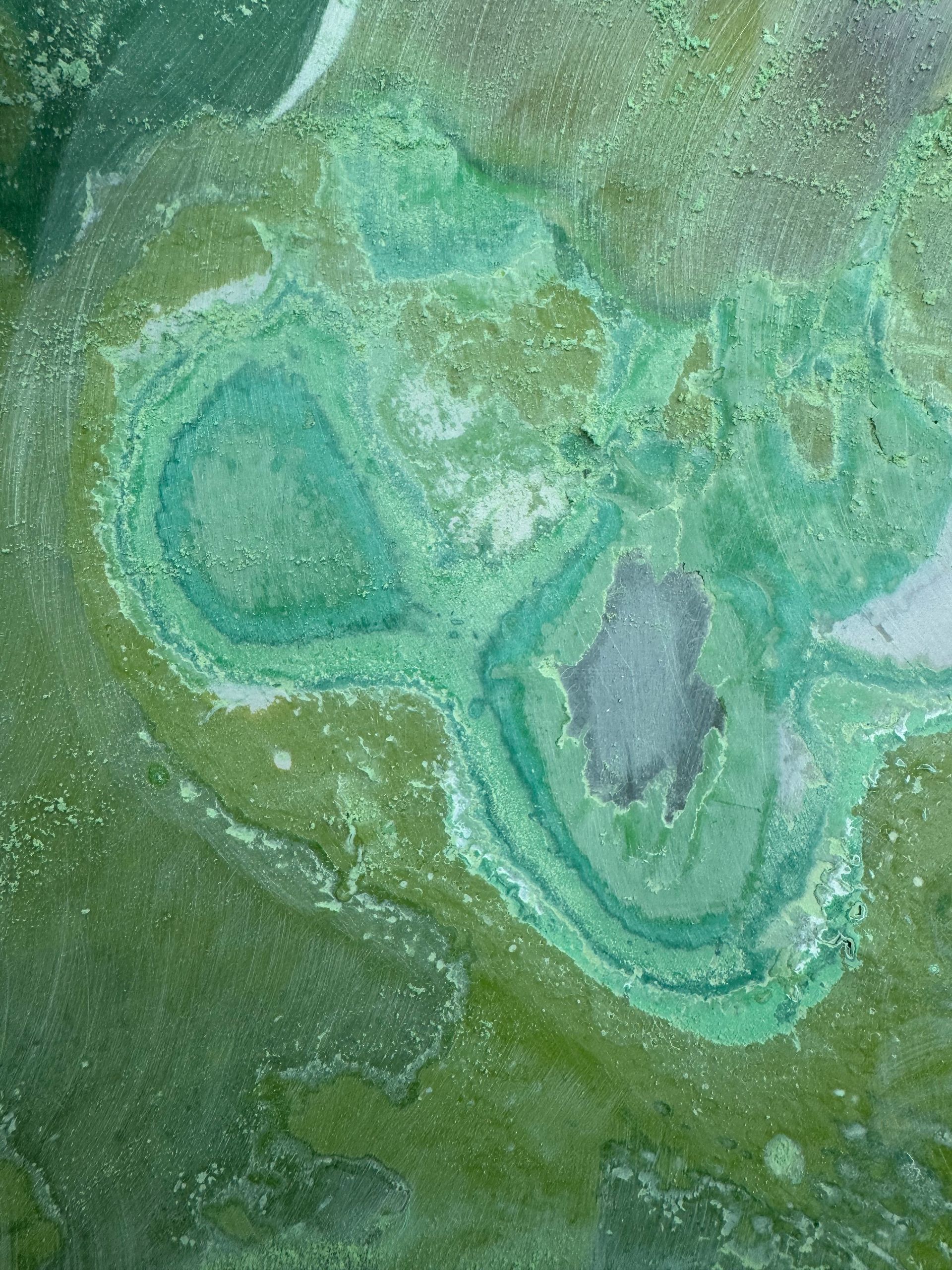 Close-up of severely deteriorated green waterslide surface showing multiple layers of failed gelcoat, peeling, and exposed fiberglass at Legoland Malaysia