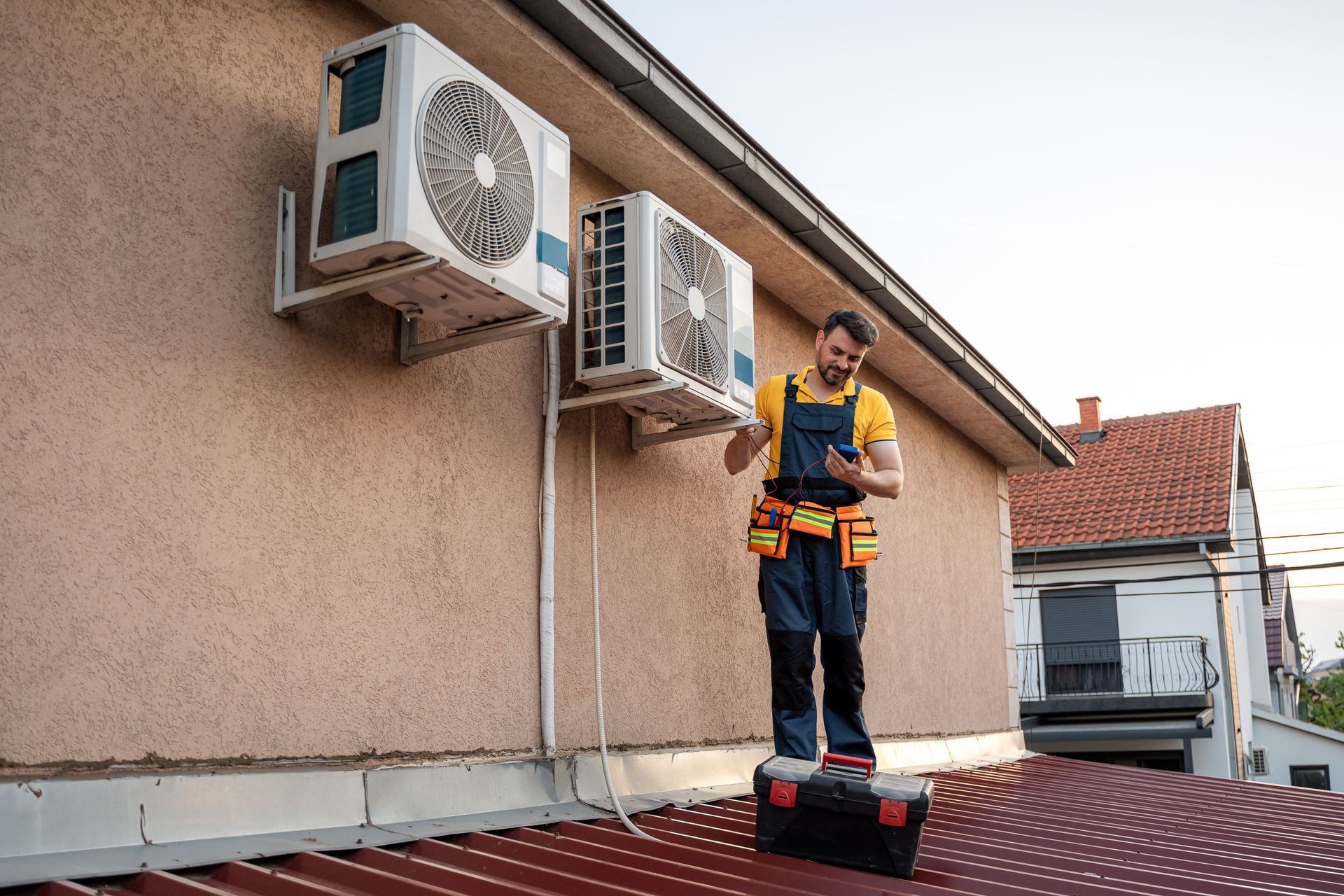 HVAC technician on roof, inspecting air conditioning unit. Technician is wearing work clothes.