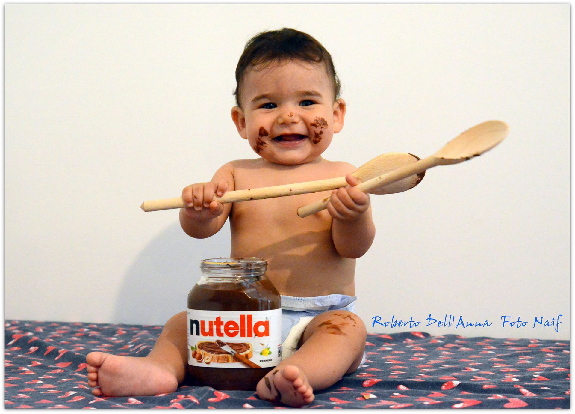 Un bambino tiene in mano un cucchiaio di legno accanto a un barattolo di nutella