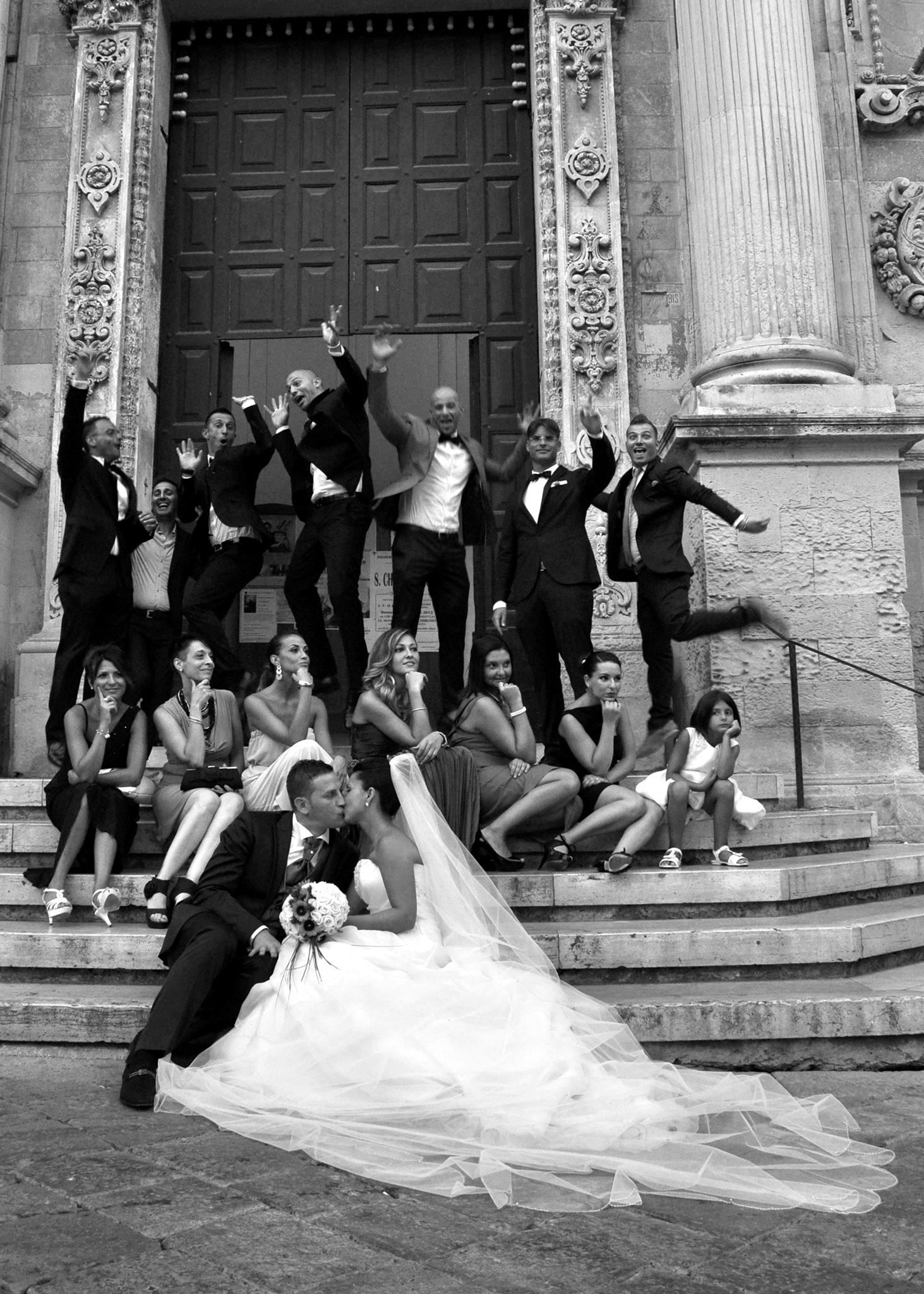 Una coppia di sposi posa per una foto con i loro invitati alle nozze sui gradini di una chiesa.