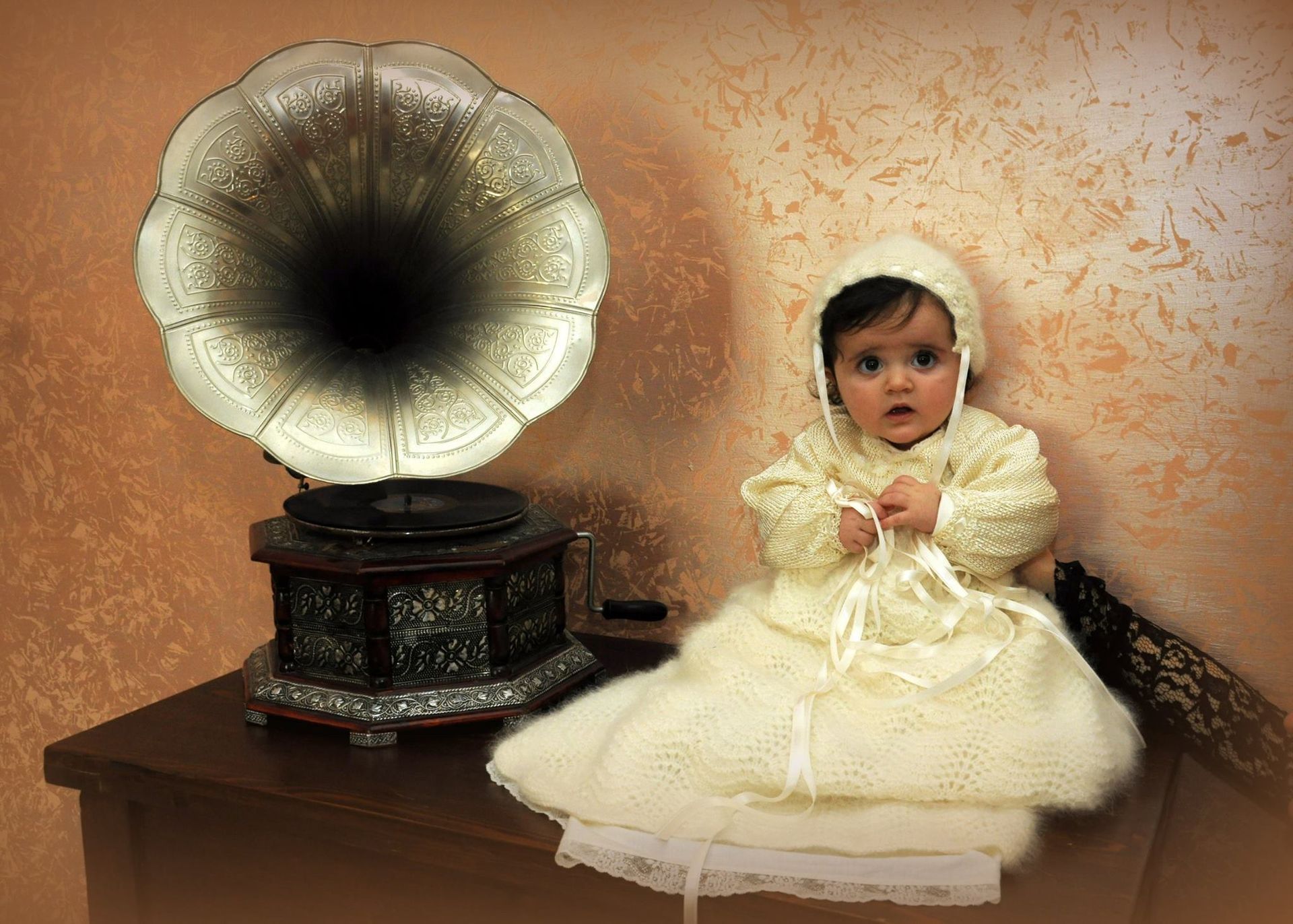 Un bambino vestito di bianco è seduto davanti a un fonografo.