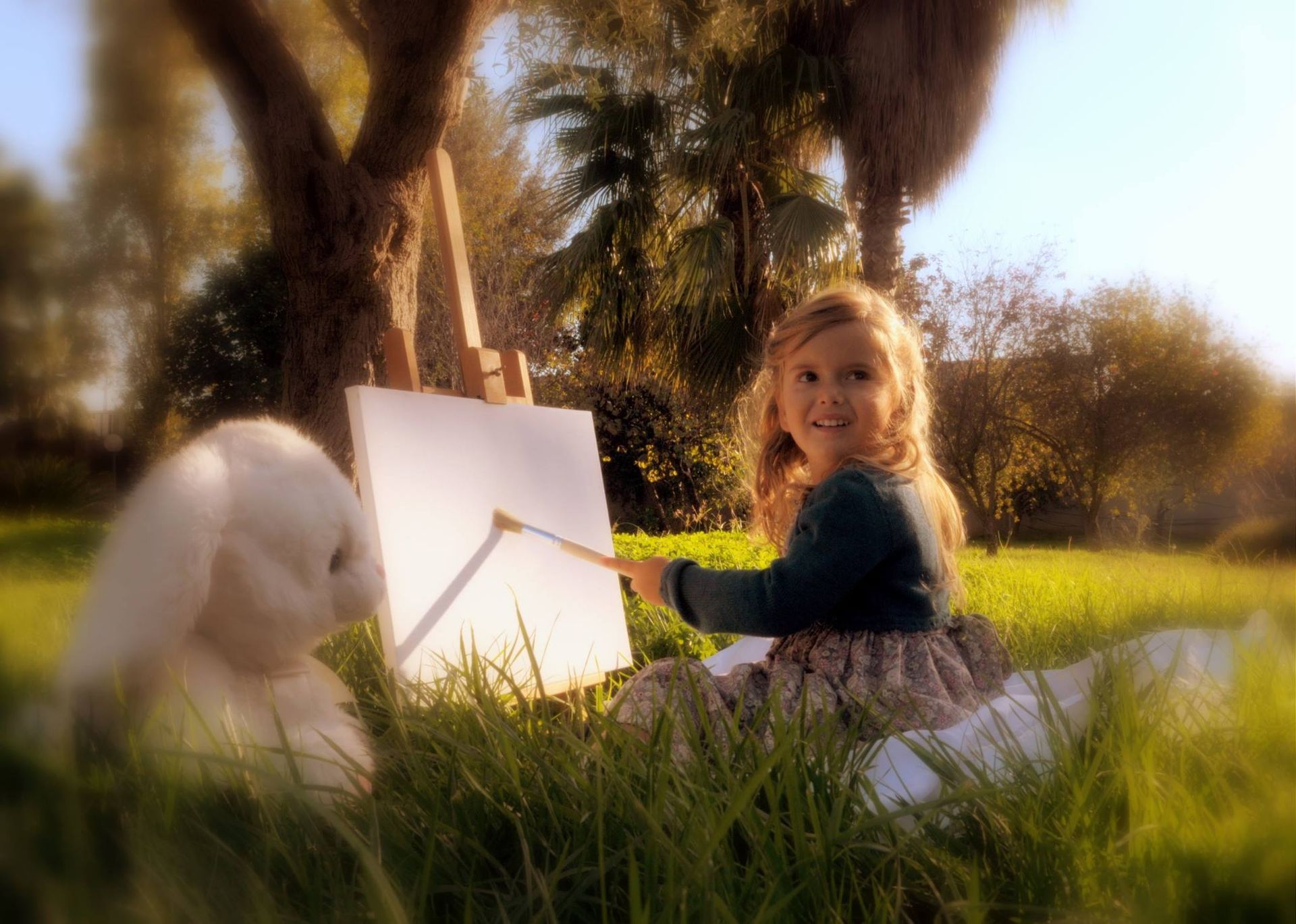 Una bambina è seduta sull'erba e dipinge su una tela.