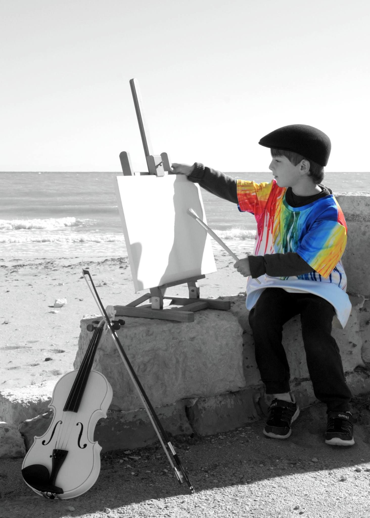 Un ragazzo con una maglietta arcobaleno sta dipingendo su un cavalletto accanto a un violino