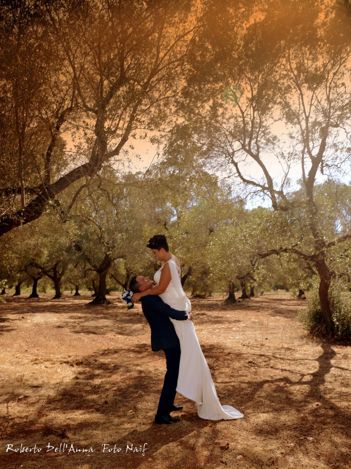 Una coppia di sposi posa per una foto in un uliveto.