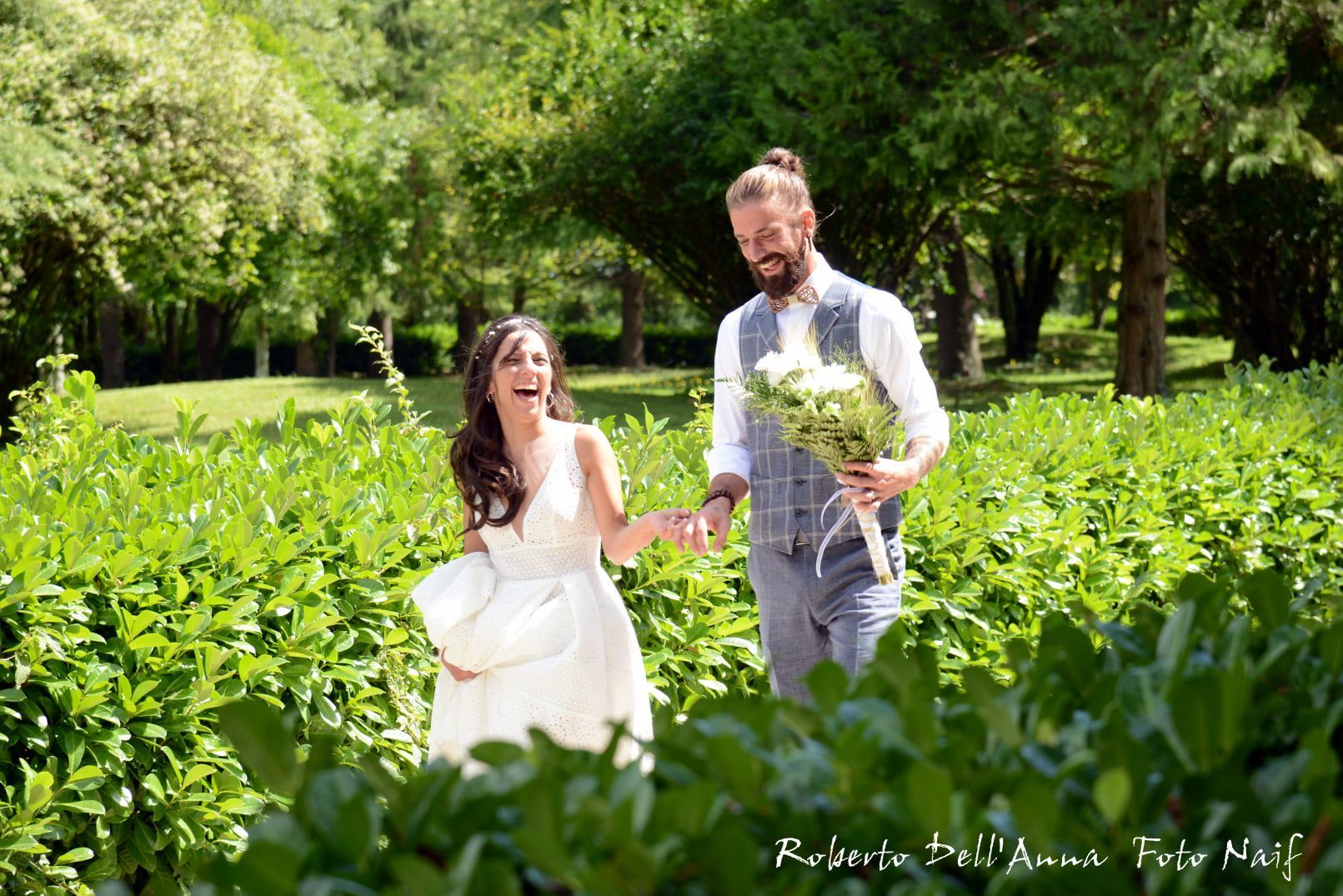 Una sposa e uno sposo si tengono per mano in un campo.