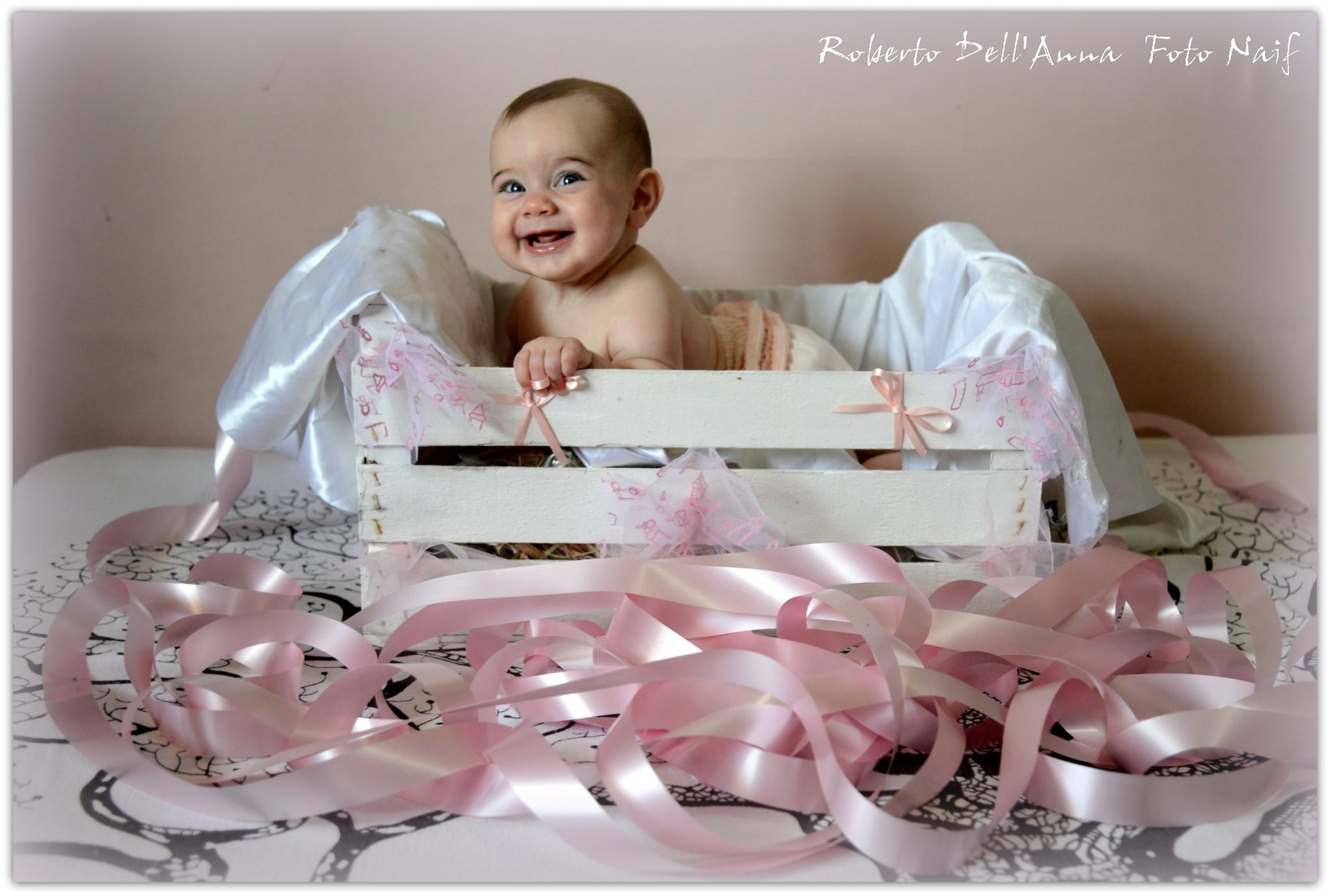 Un bambino è sdraiato in una cassa di legno con nastri rosa intorno