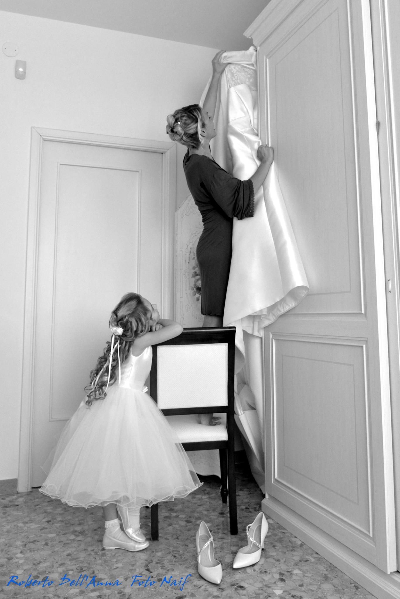 Una foto in bianco e nero di una donna che appende un abito da sposa a una parete.