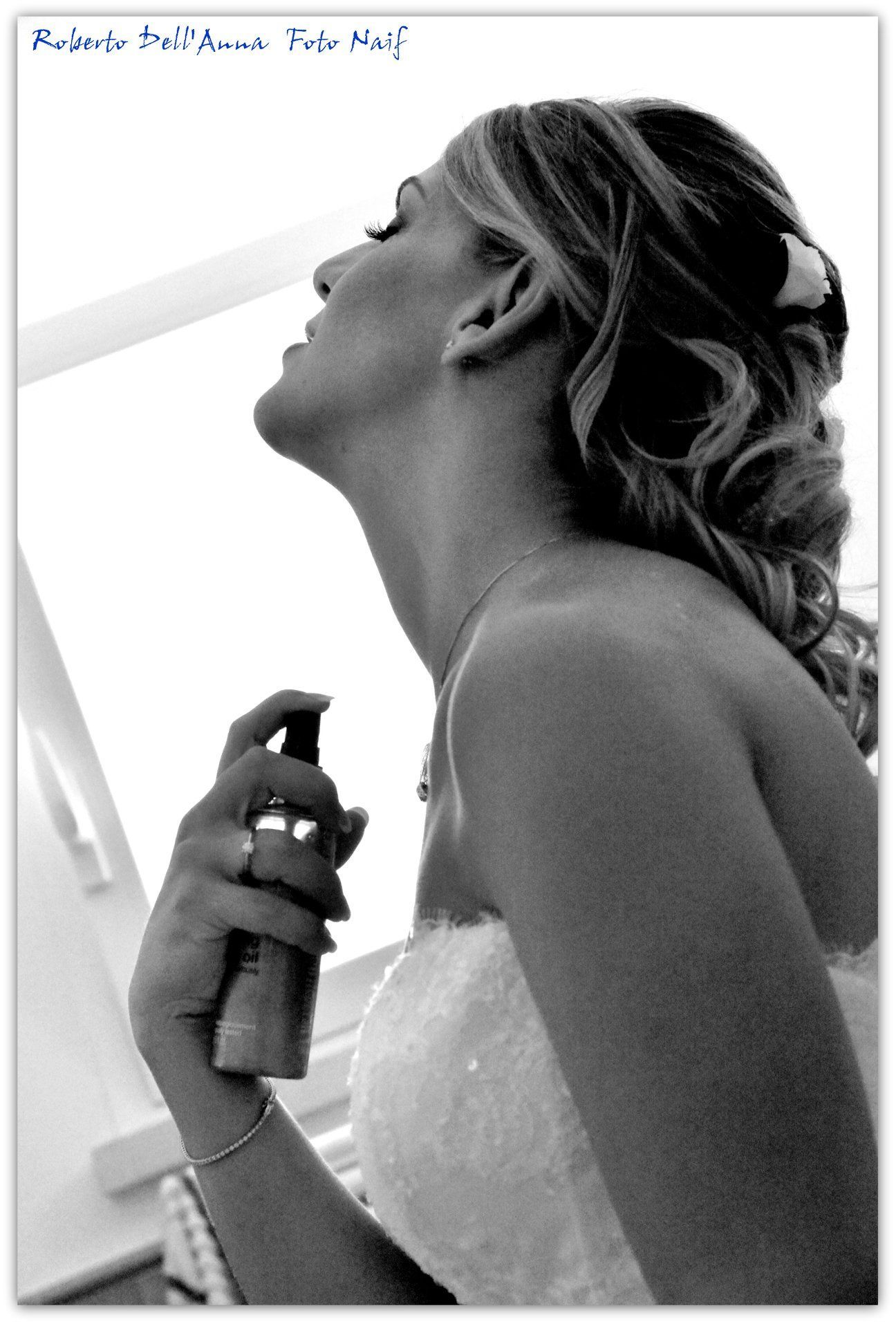 Una donna in abito da sposa si spruzza i capelli con uno spruzzatore