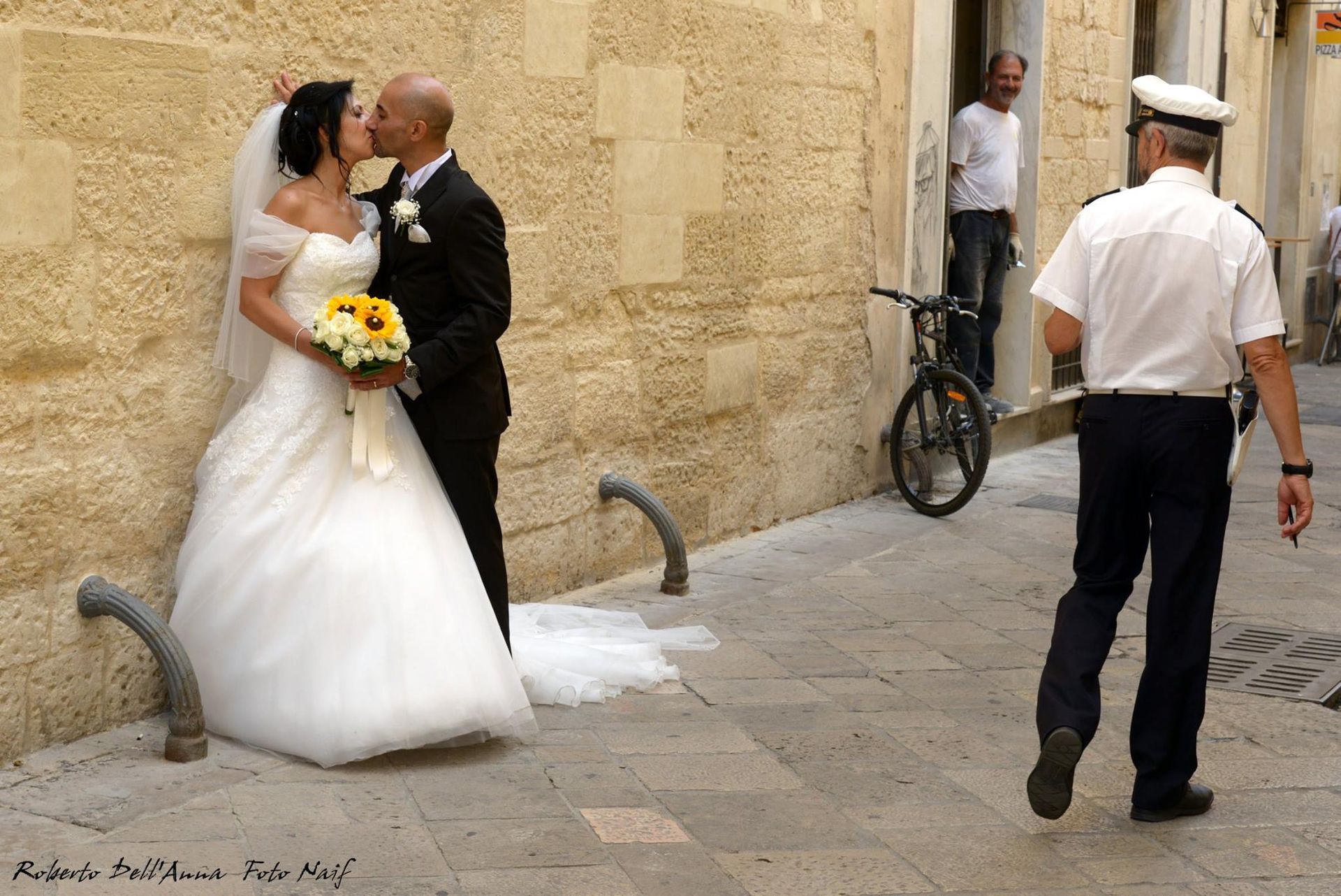 Una sposa e uno sposo che si baciano davanti a un agente di polizia