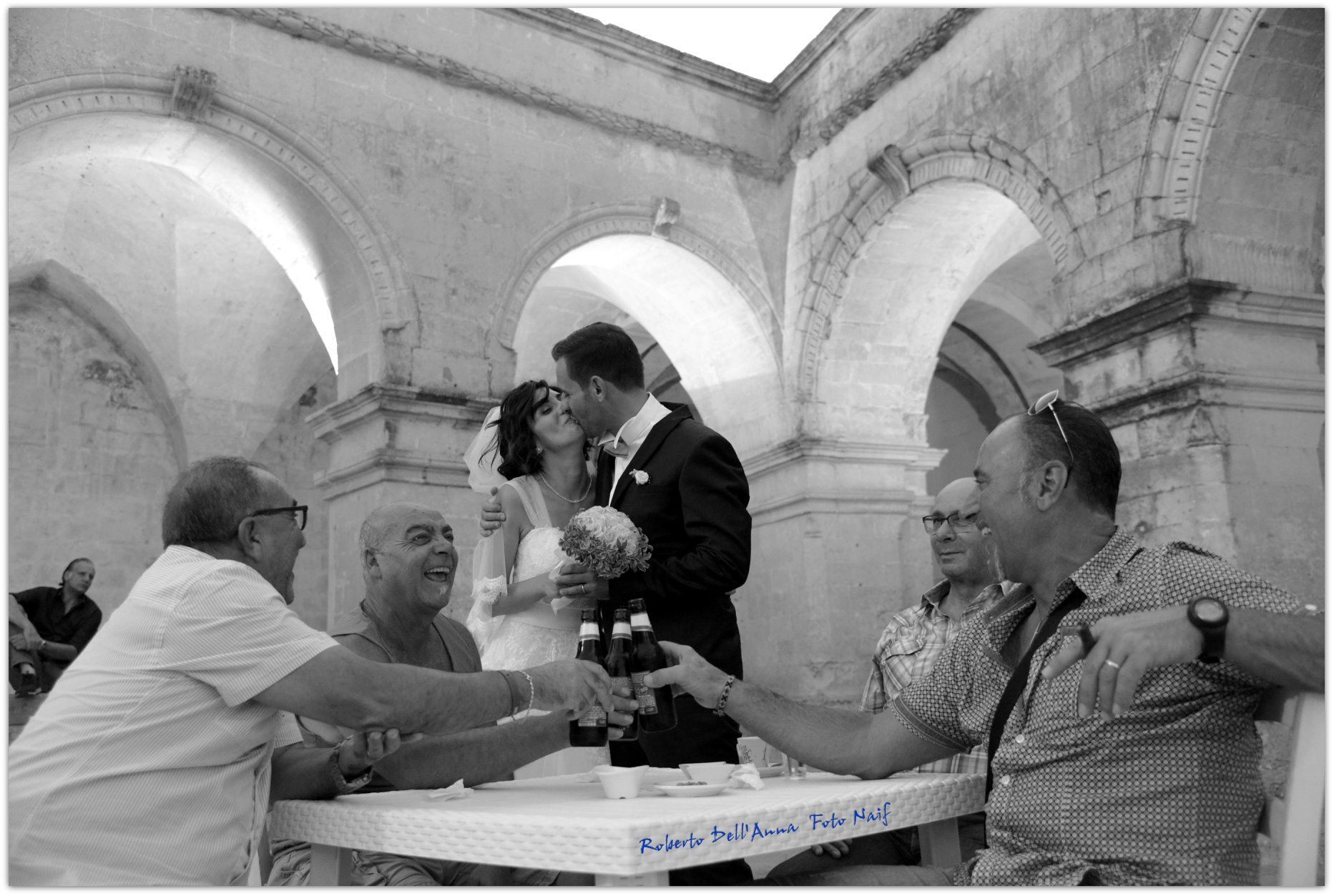 Una sposa e uno sposo si baciano seduti a un tavolo con un gruppo di uomini.