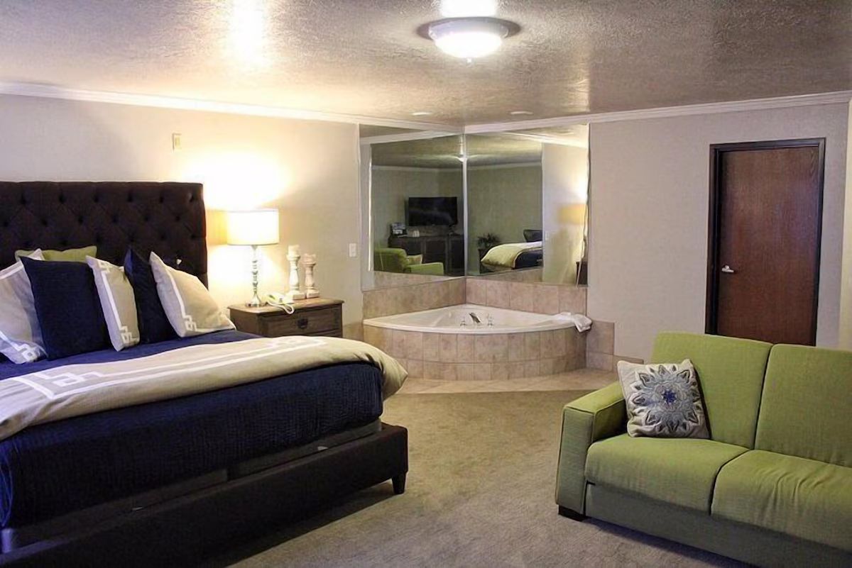Bedroom with bed, hot tub, and green sofa. Mirror on wall, door on right.