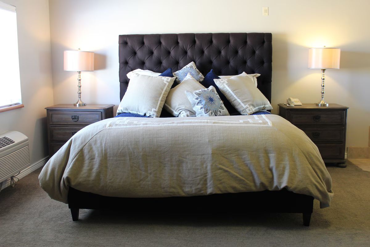Bedroom with bed, tufted headboard, nightstands, lamps, and beige bedding.