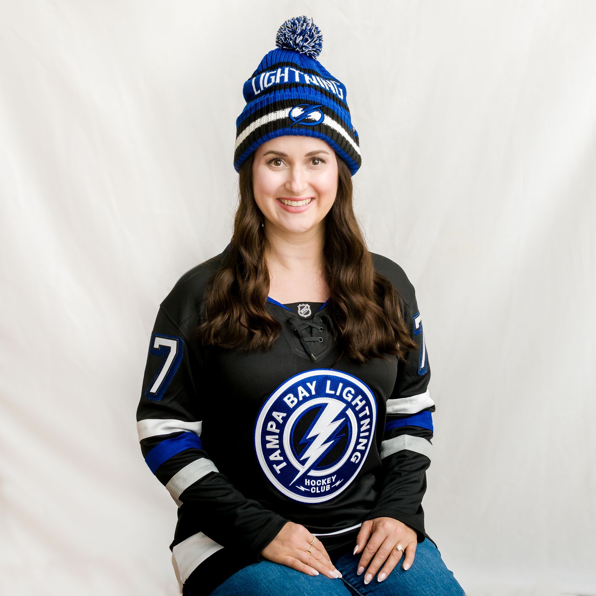 Woman wearing a Tampa Bay Lightning jersey and hat smiles. Blue and black colors.