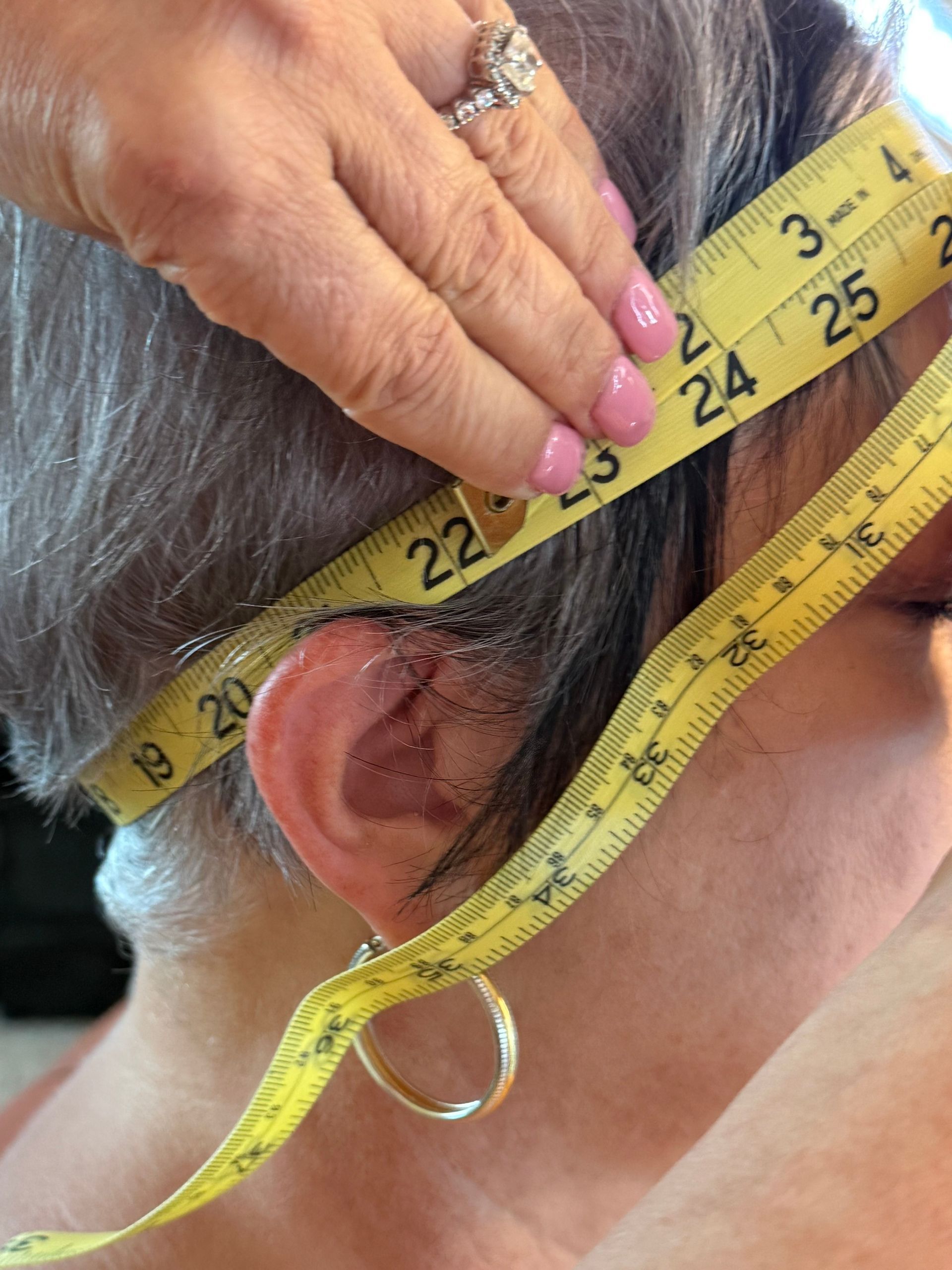 A person's hands sewing hair onto a wig cap. Three mannequin heads with wigs are in the background.