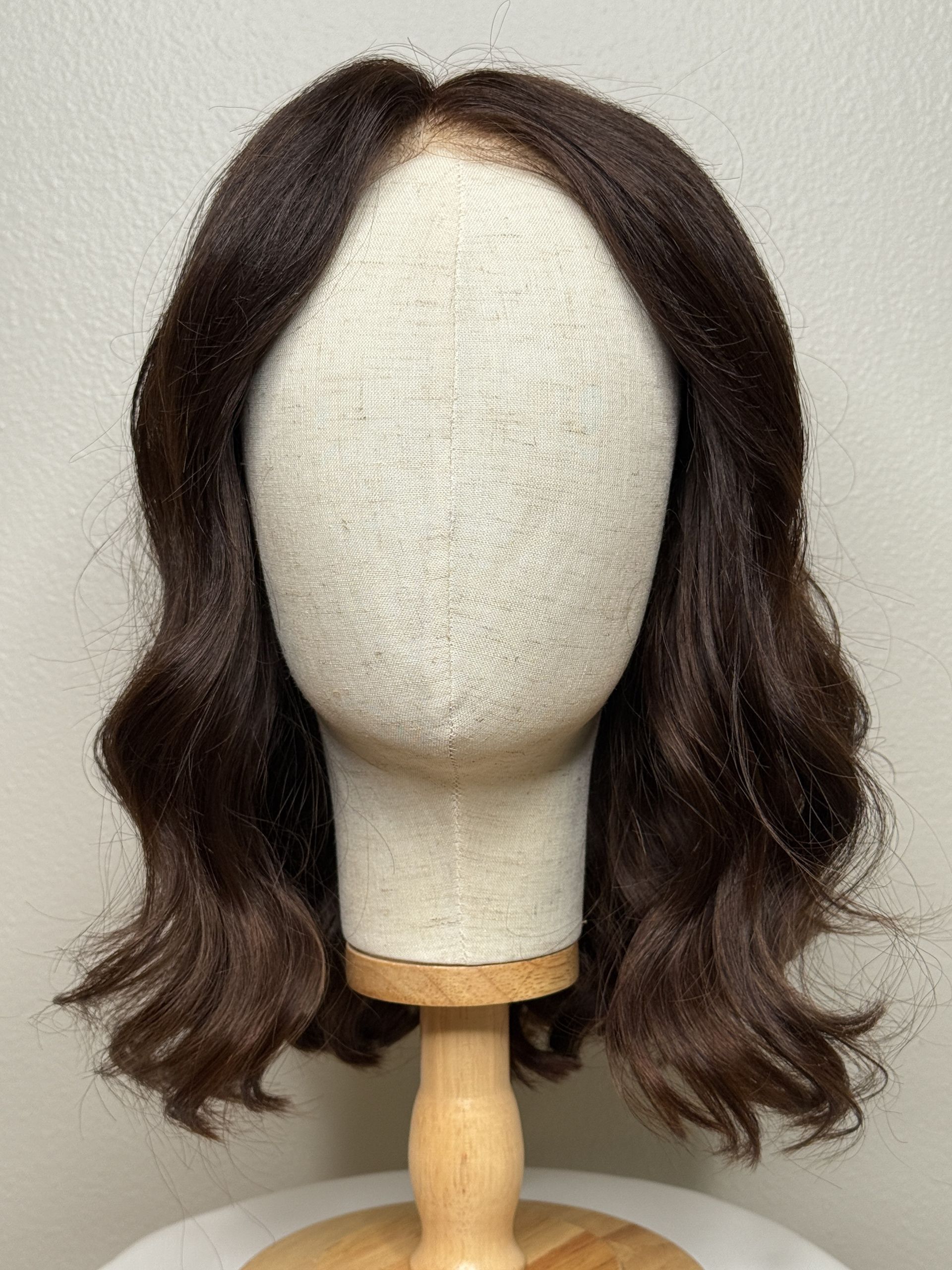 Dark brown wig on a mannequin head with wavy texture and a natural-looking part.