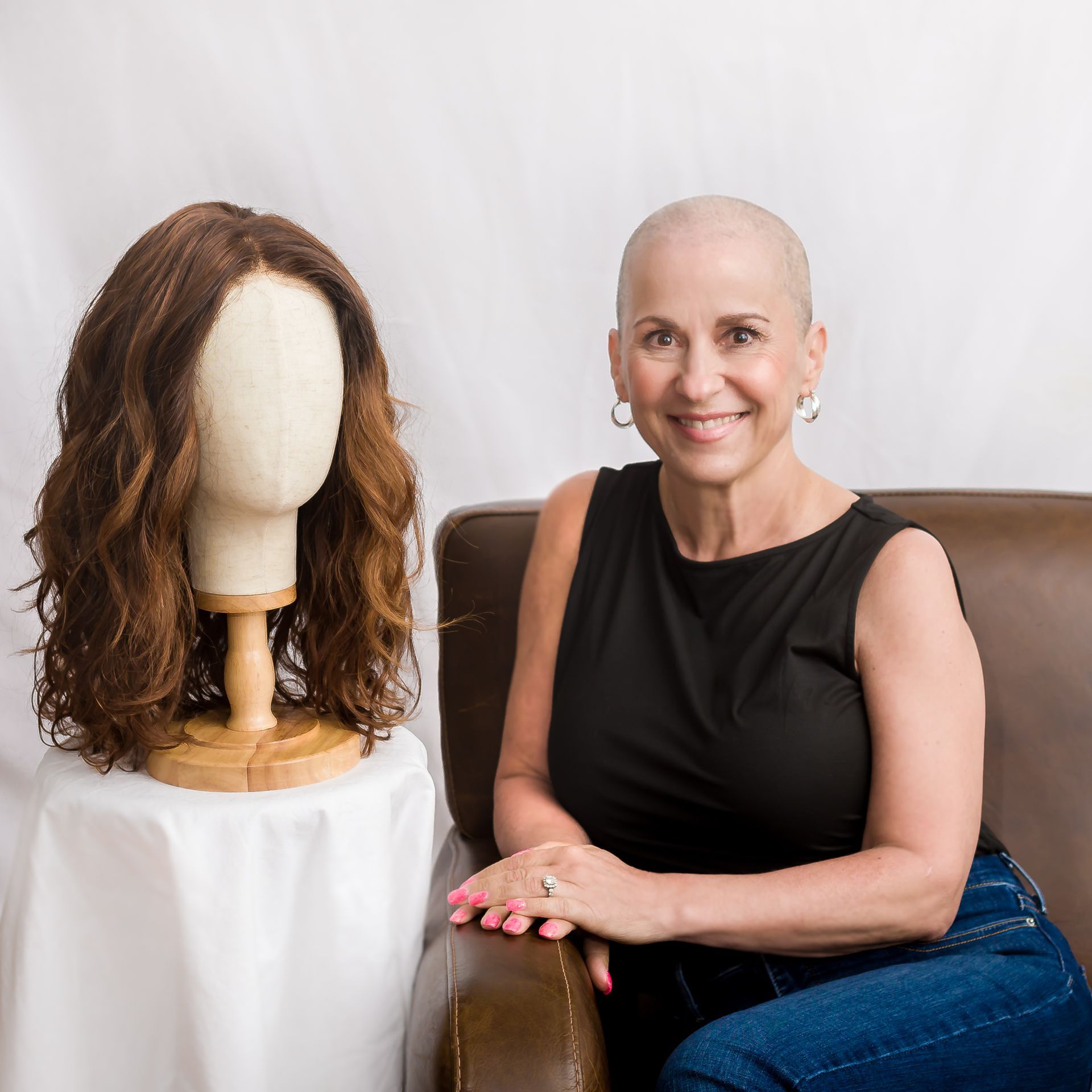 Woman in white shirt holding hair color swatches, working on laptop at a table.