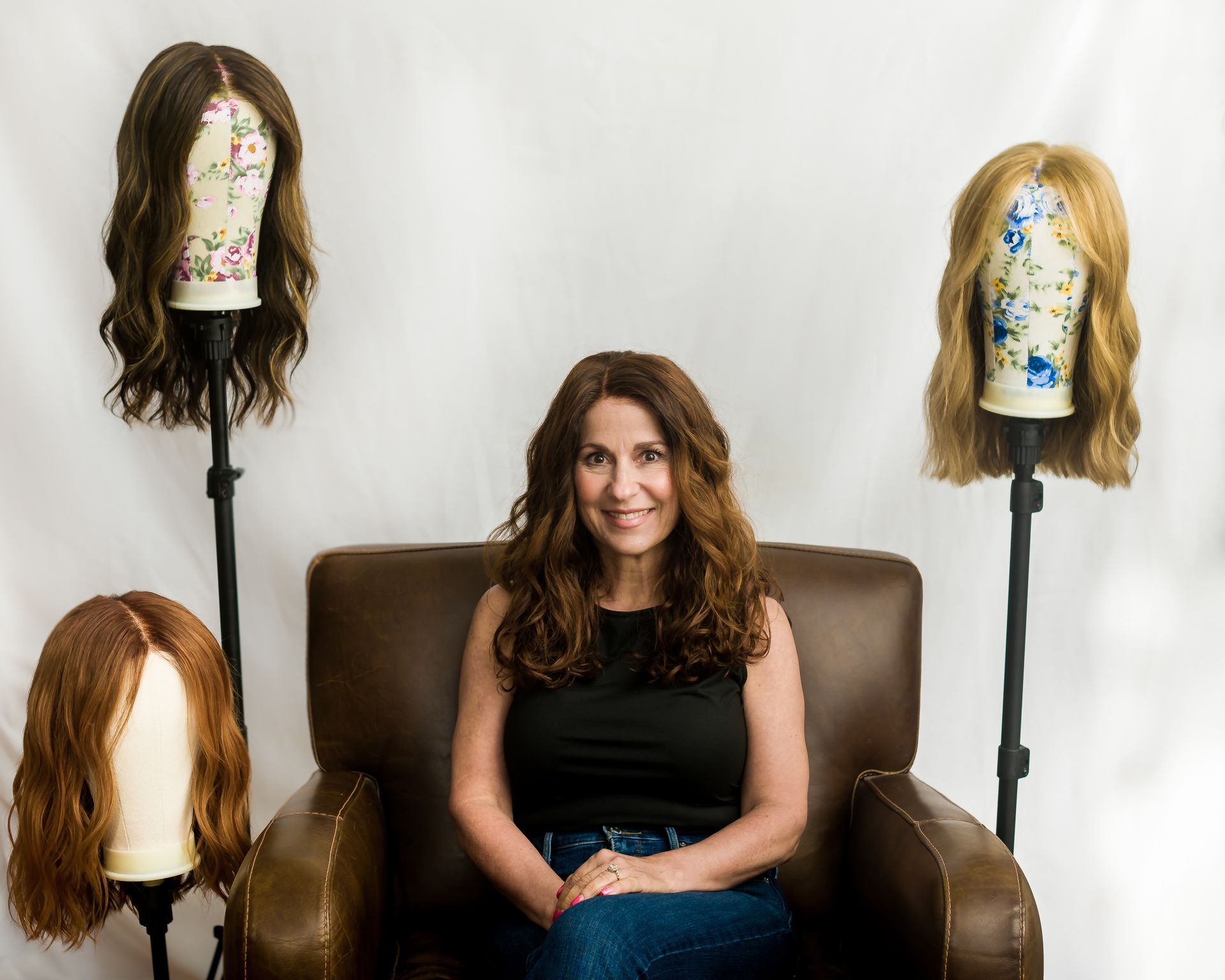 Woman with long brown hair smiles, wearing a beige sweater outdoors.