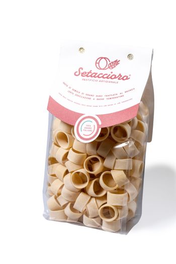 Sacchetto trasparente di pasta arrotolata beige con etichetta rosa e bianca su sfondo bianco.