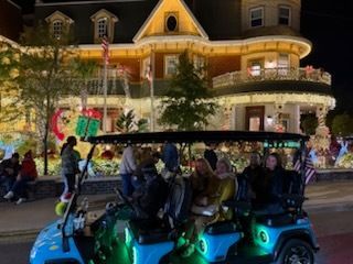 People in a decorated golf cart in front of a brightly lit building at night.