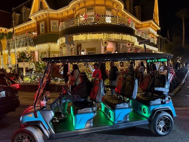 A blue golf cart with passengers driving on a street decorated for Christmas; a building is in the background.