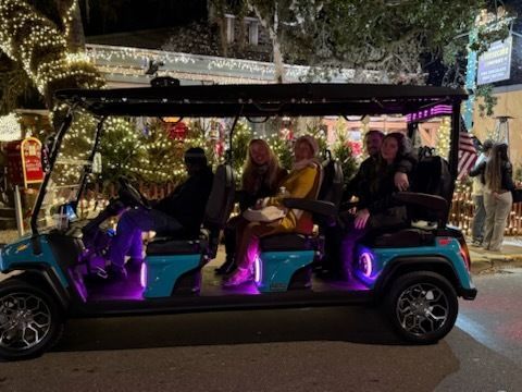 Blue golf cart with passengers, lit up with purple lights, driving on a street at night.
