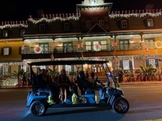 Golf cart with passengers in front of a decorated building at night.