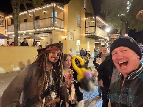 People pose for photo with Jack Sparrow in a lit-up, old-style building setting. One smiles wide.