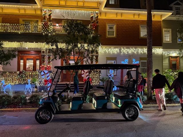 A teal golf cart parked in front of a decorated house with people walking nearby, Christmas lights are visible.