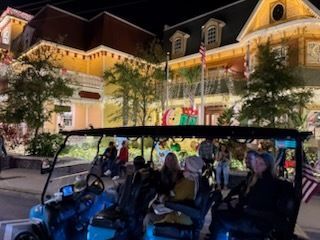 Golf cart with people in front of decorated buildings at night.