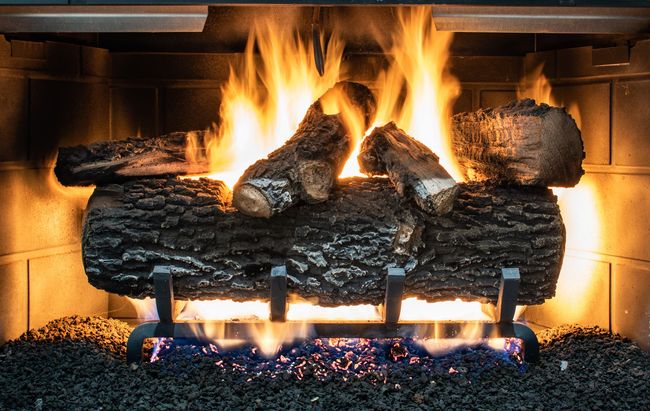 A fireplace filled with logs and flames is lit up at night.