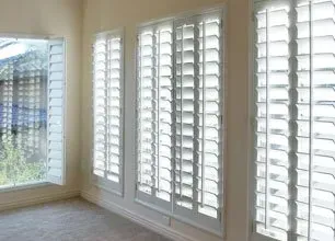 A room with a lot of white shutters on the windows.