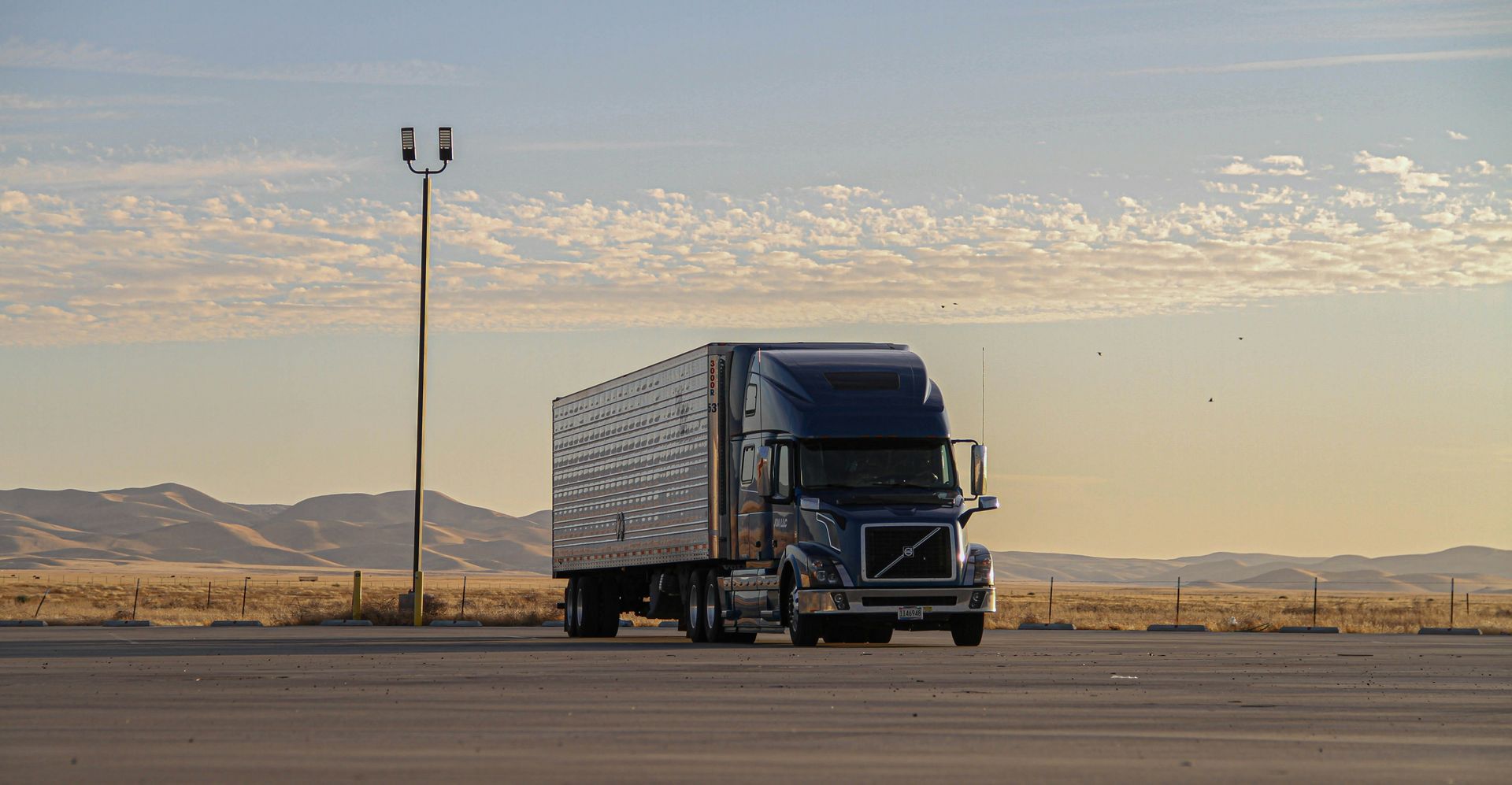 A blue semi truck is driving down a desert road.