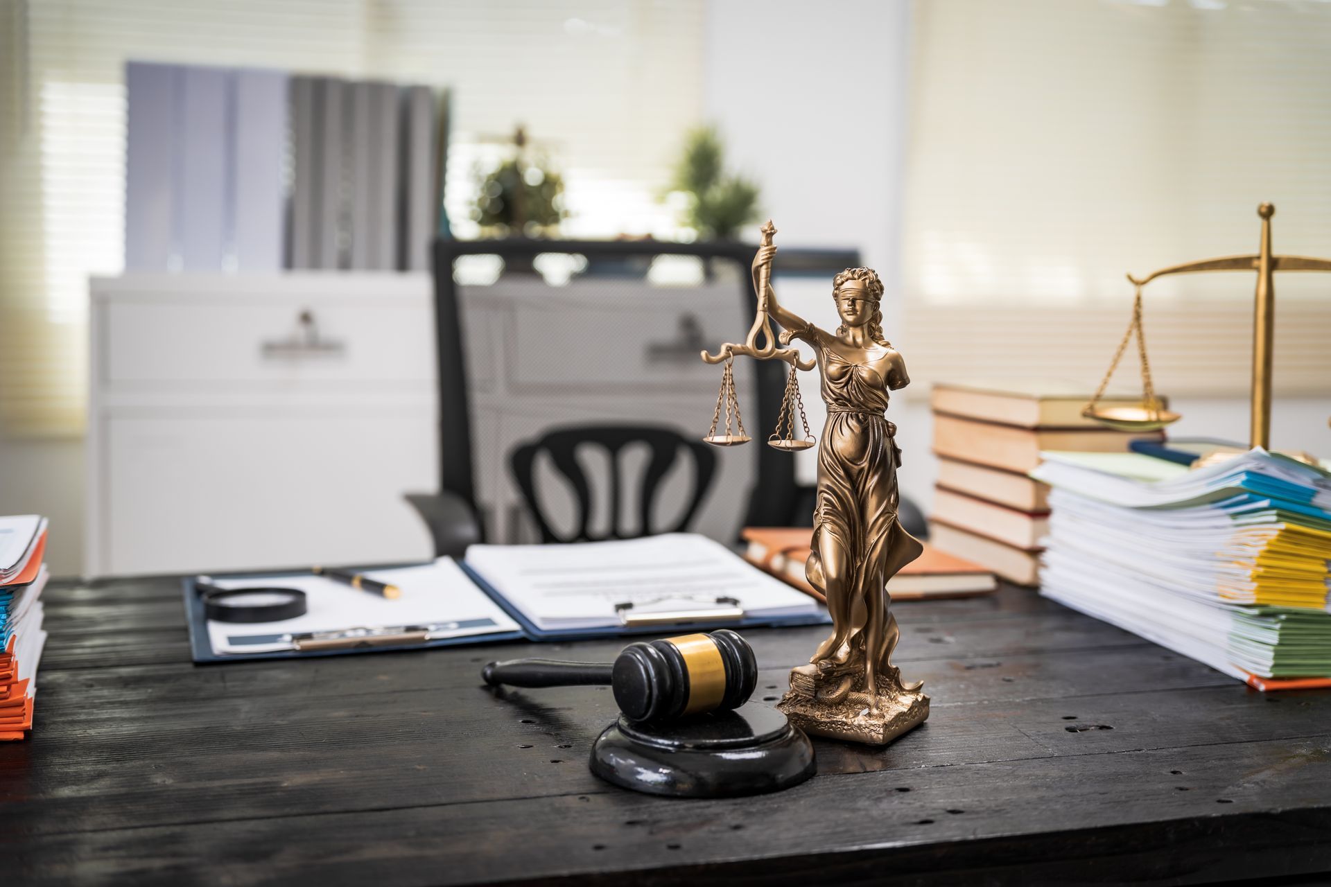 A law office desk with scales of justice statue, gavel, documents, and books.