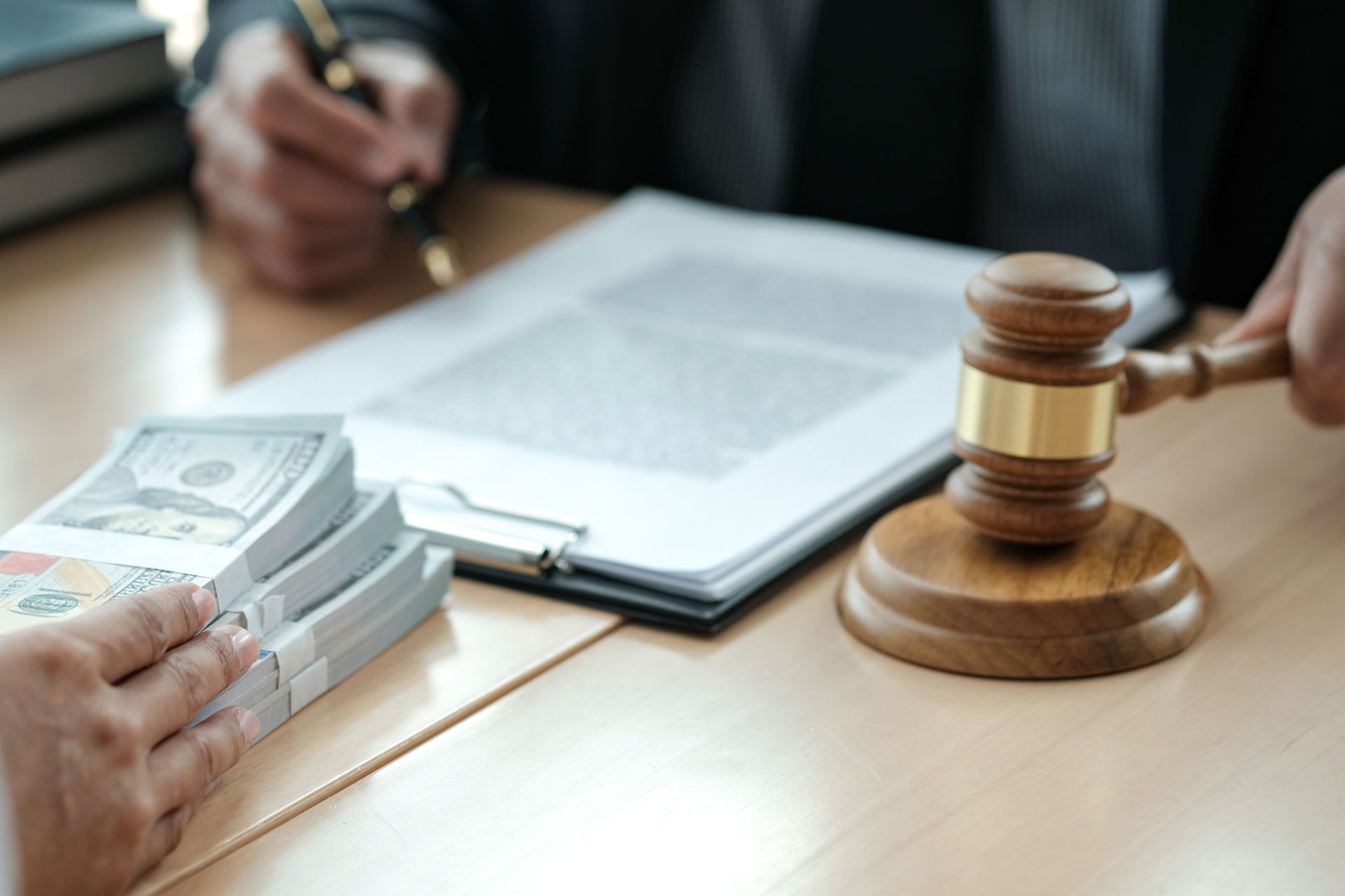 Person handing cash near a judge's gavel and legal documents. Person handing cash near a judge's gavel and legal documents.