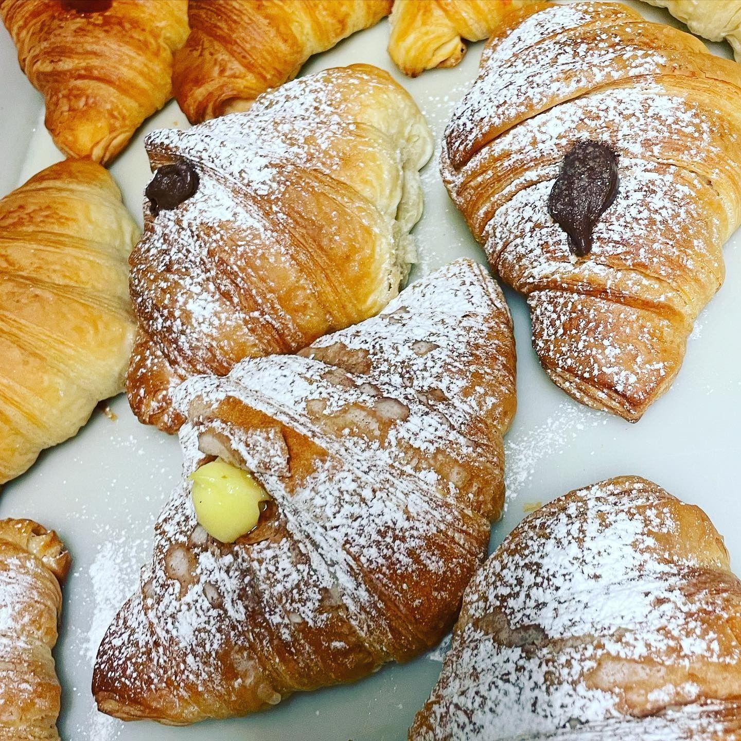 Cornetti spolverati con zucchero a velo, alcuni farciti con cioccolato o panna.