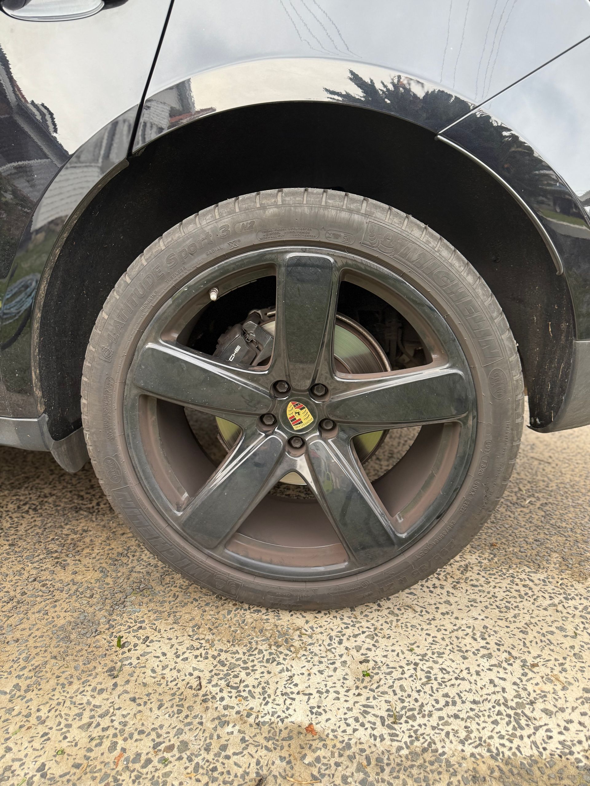 Black Porsche wheel on a black vehicle, parked on a paved surface.