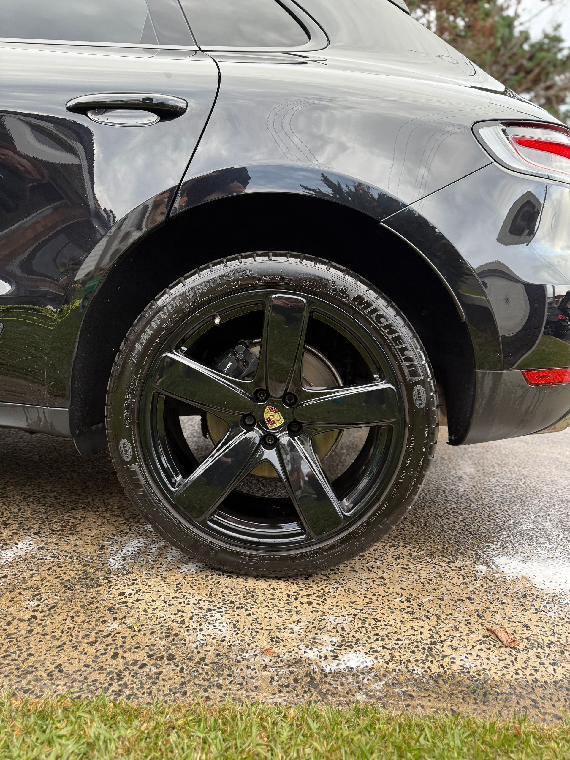 Black Porsche Macan SUV, side view of rear tire. Black rim with shiny black paint, set on wet pavement.